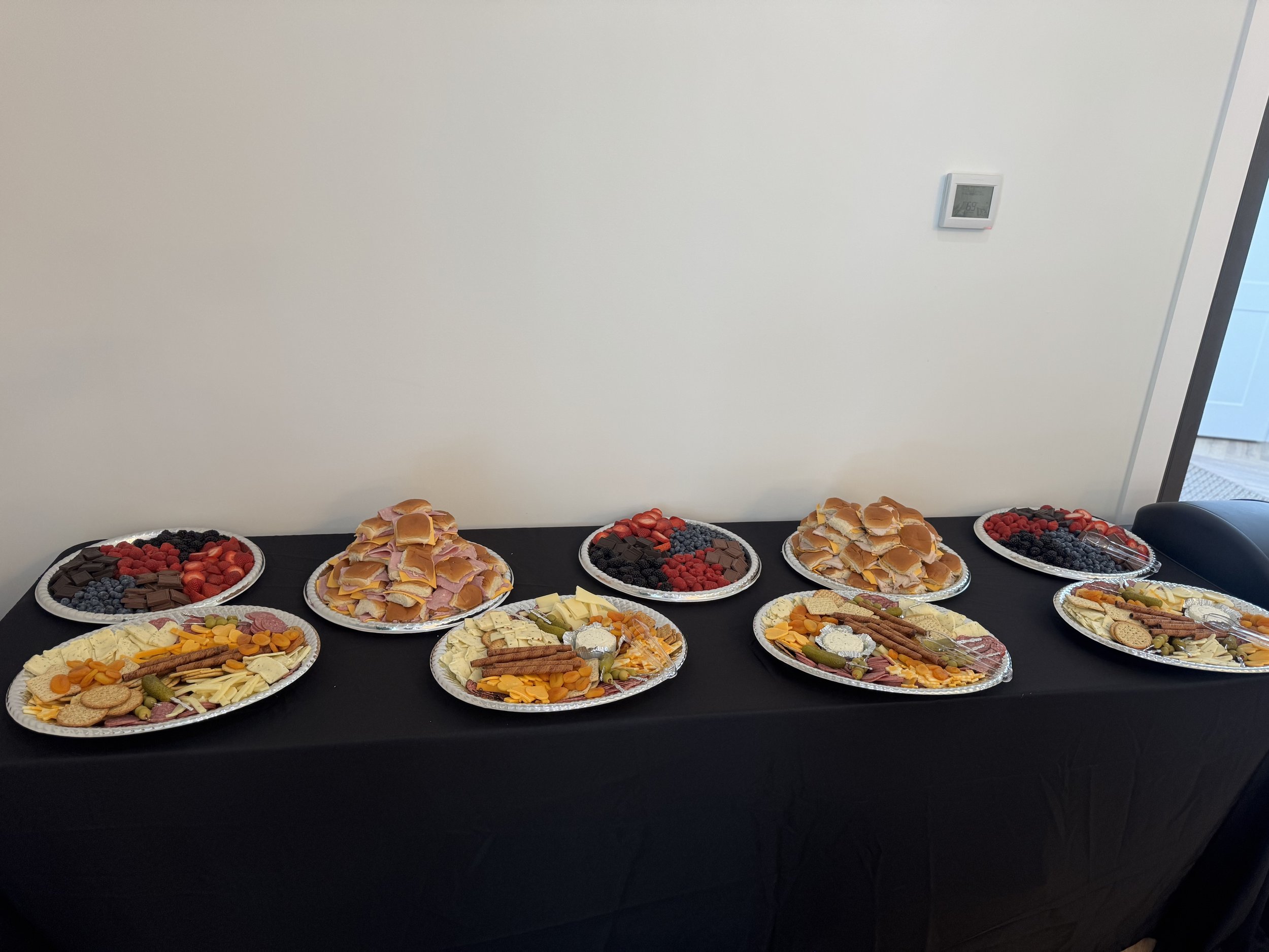 Assorted trays of snacks including cheese and crackers, cookies, fruit, chips, almonds, and an assortment of berries on a black table.