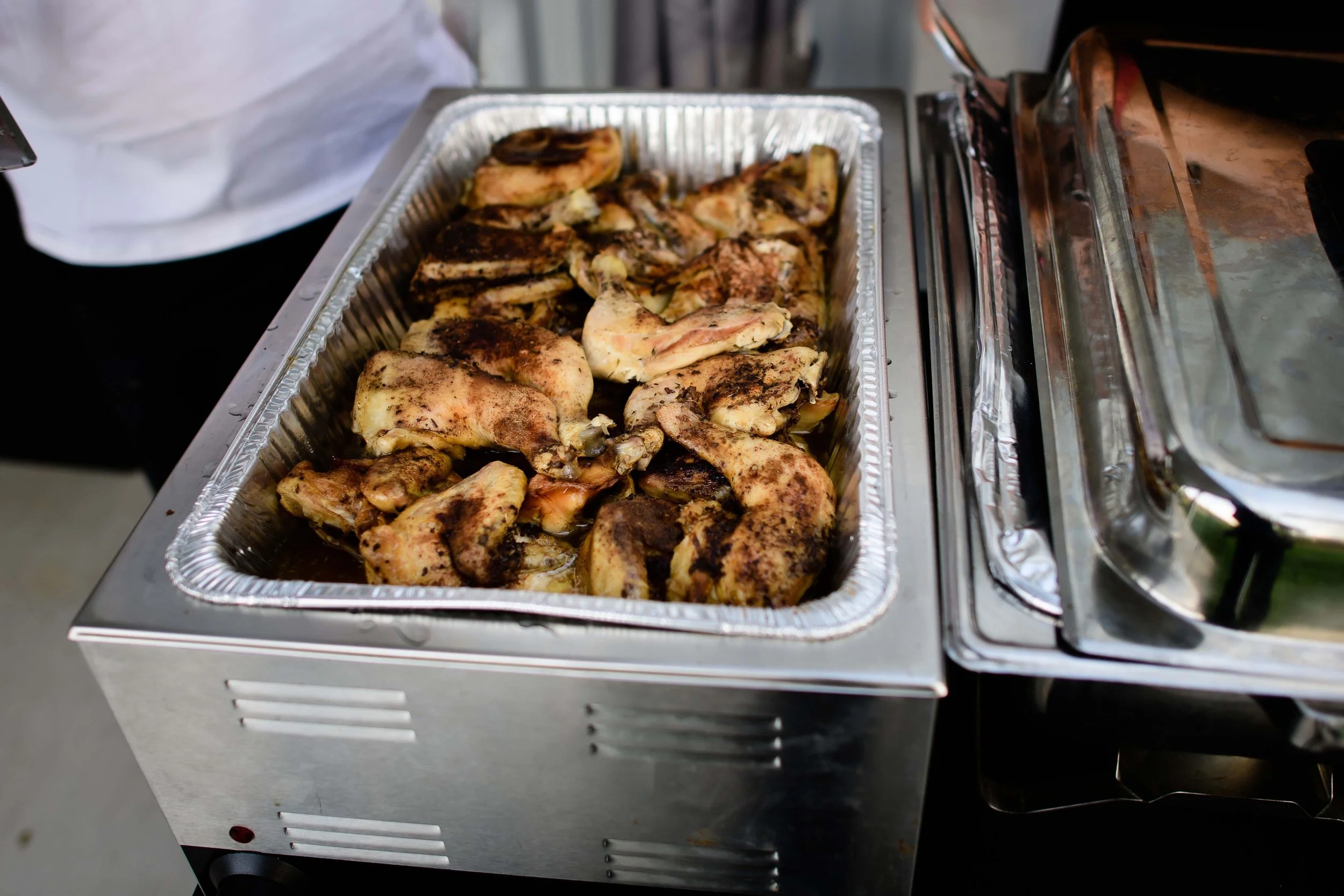 Cooked chicken pieces in a foil tray on a food warmer.