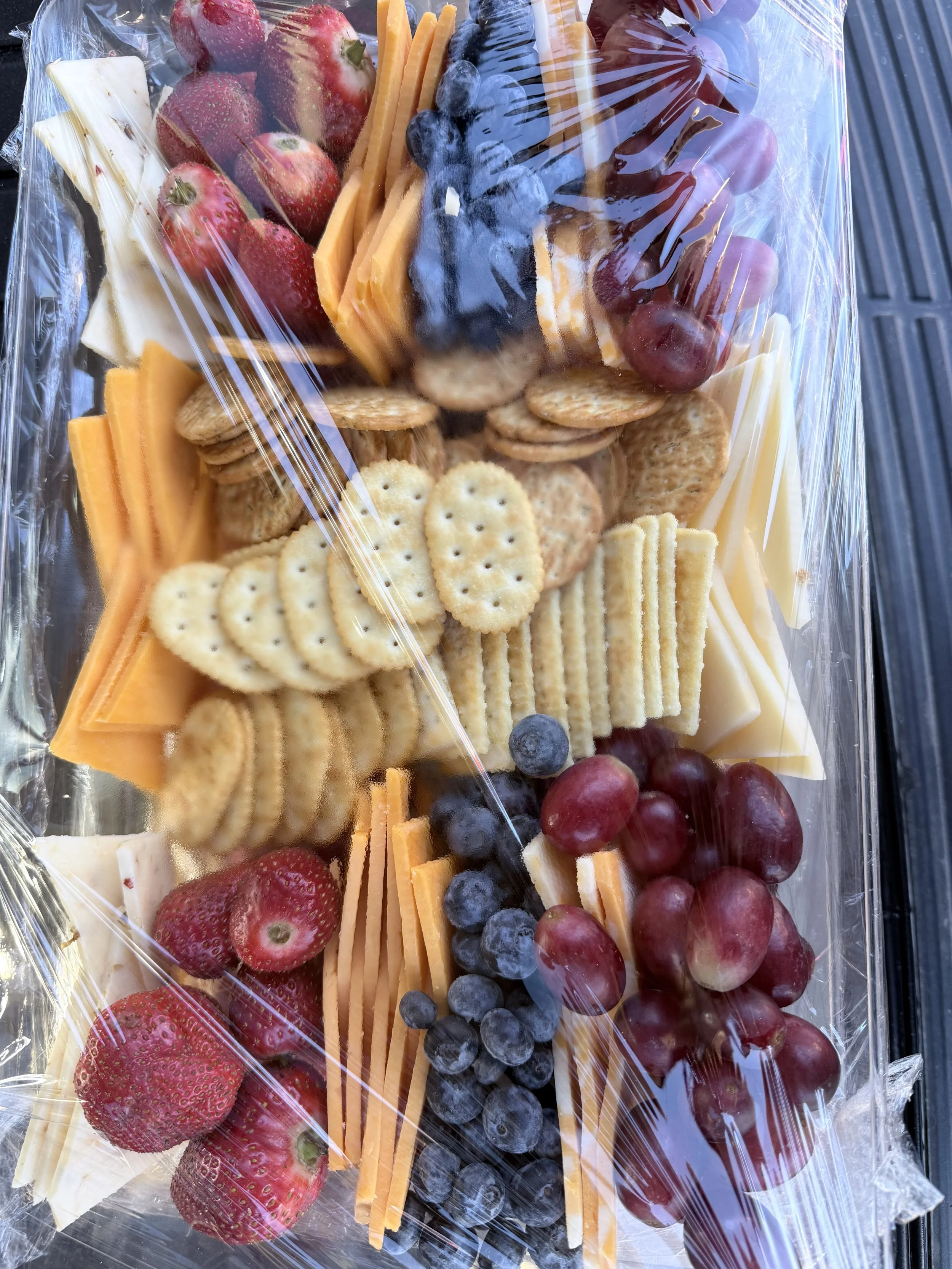 Assorted cheese, strawberries, blueberries, grapes, and crackers packed in a clear plastic wrap.