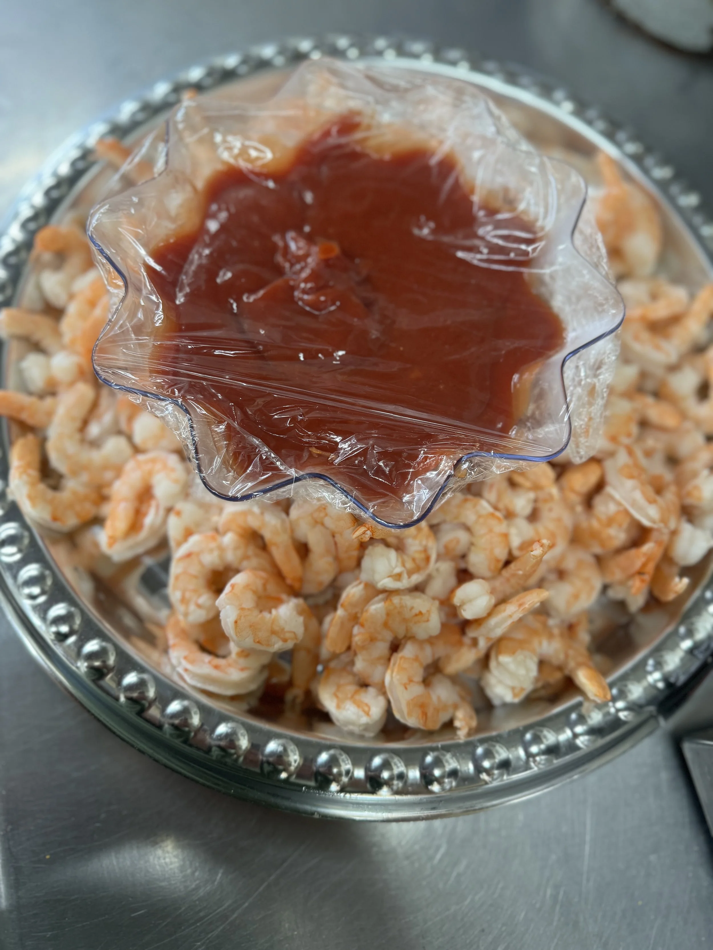 A glass bowl of cooked small shrimp with a side of cocktail sauce in a clear, star-shaped plastic container.