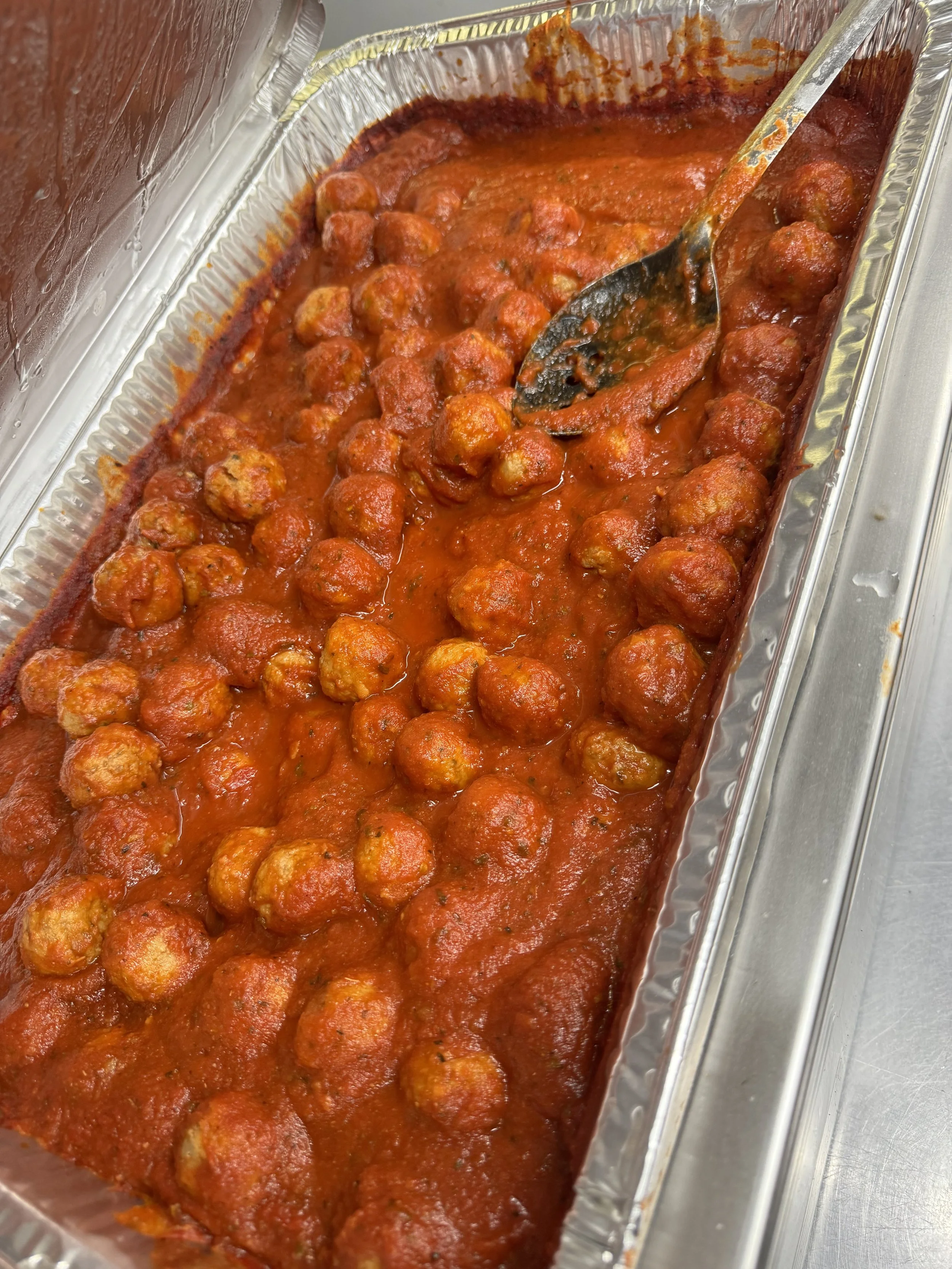 Tray of cooked meatballs in marinara sauce with a spoon.