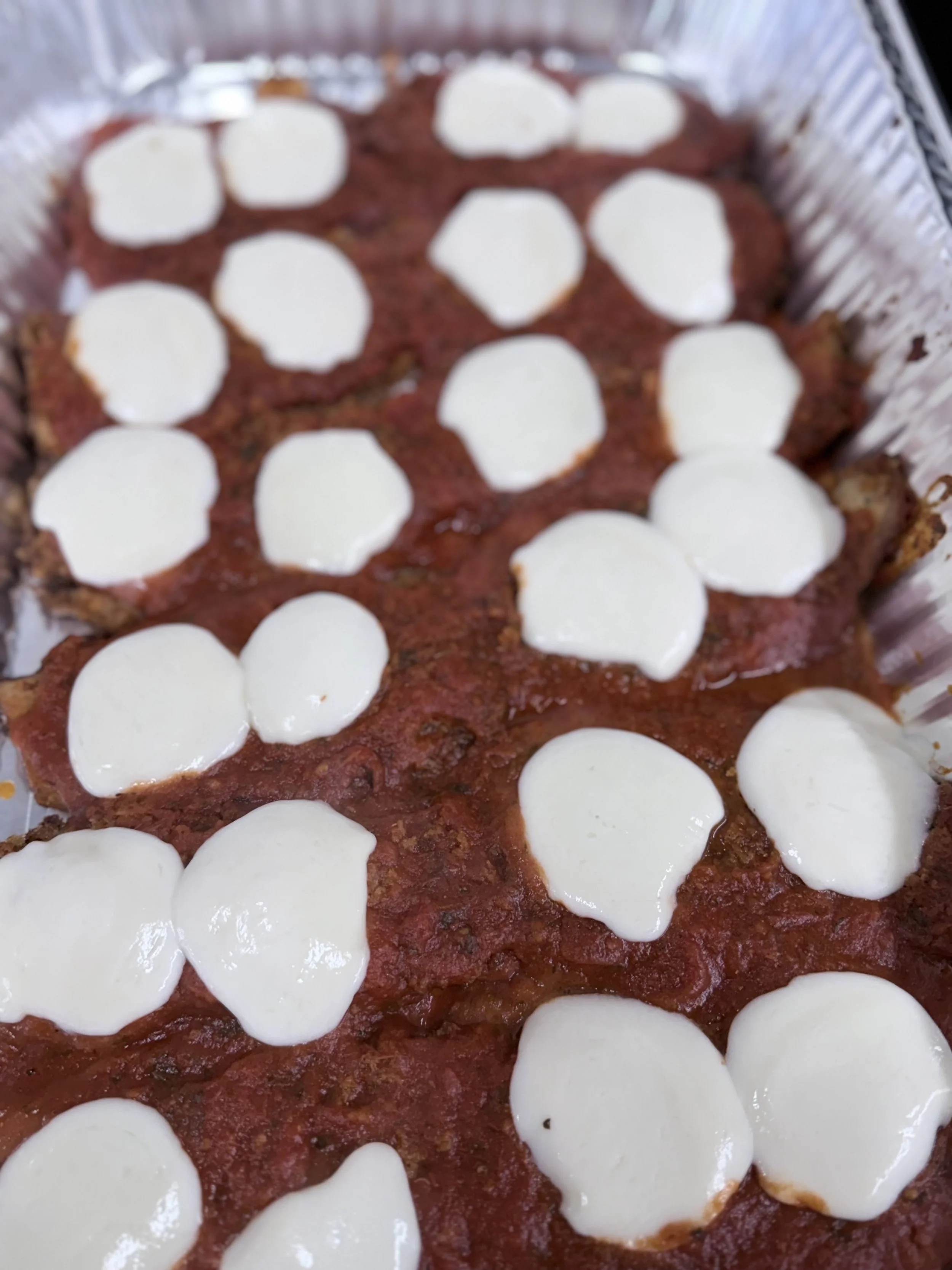 Baked eggplant parmesan topped with mozzarella cheese slices in an aluminum tray.