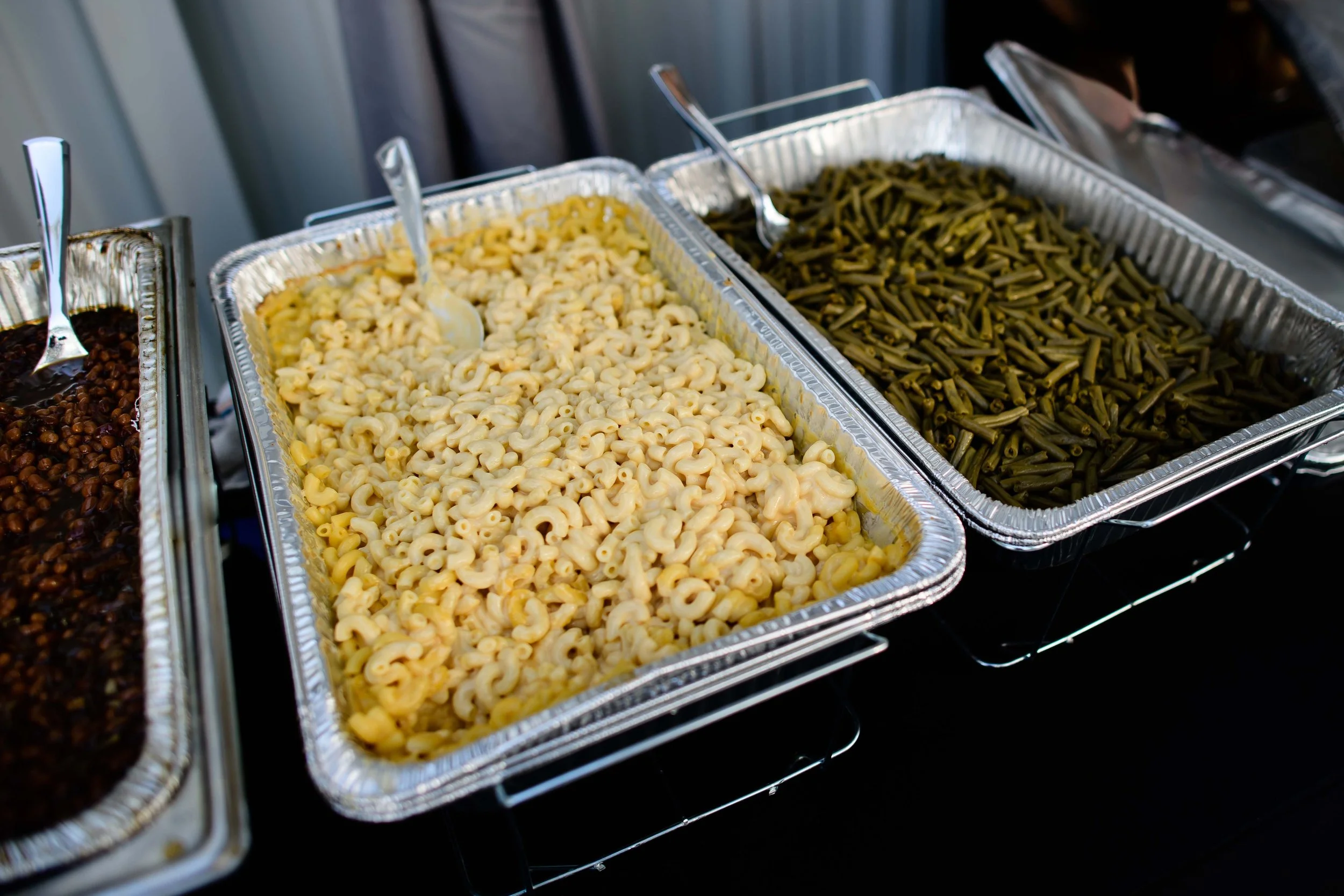 Trays of cooked macaroni and green beans at a buffet.