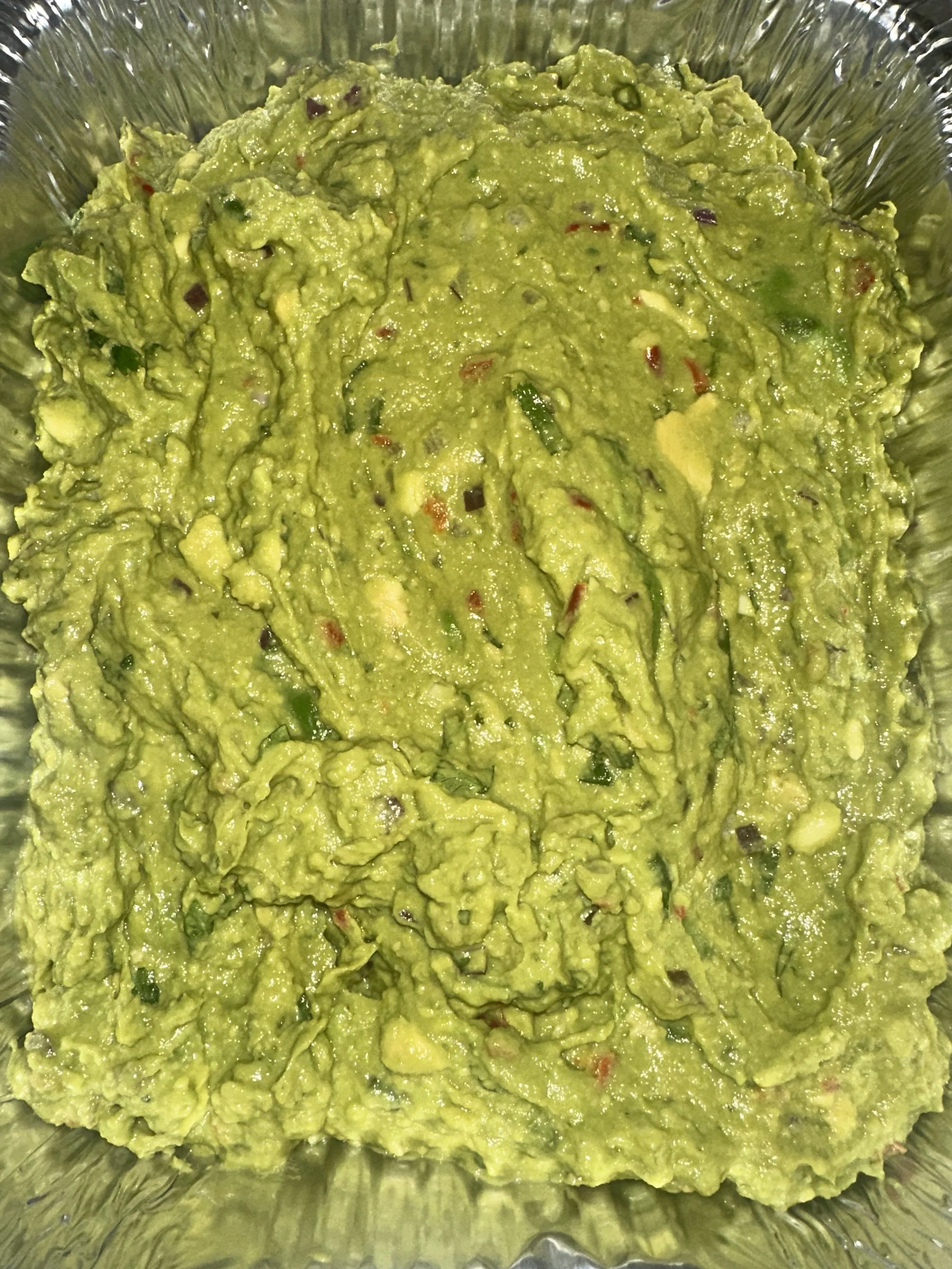 Close-up of mashed avocado with small bits of chopped onion and red pepper in a glass dish.