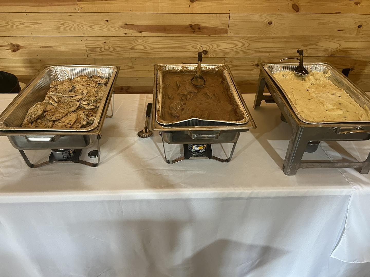 Buffet with three chafing dishes containing chicken, beef stew, and mashed potatoes