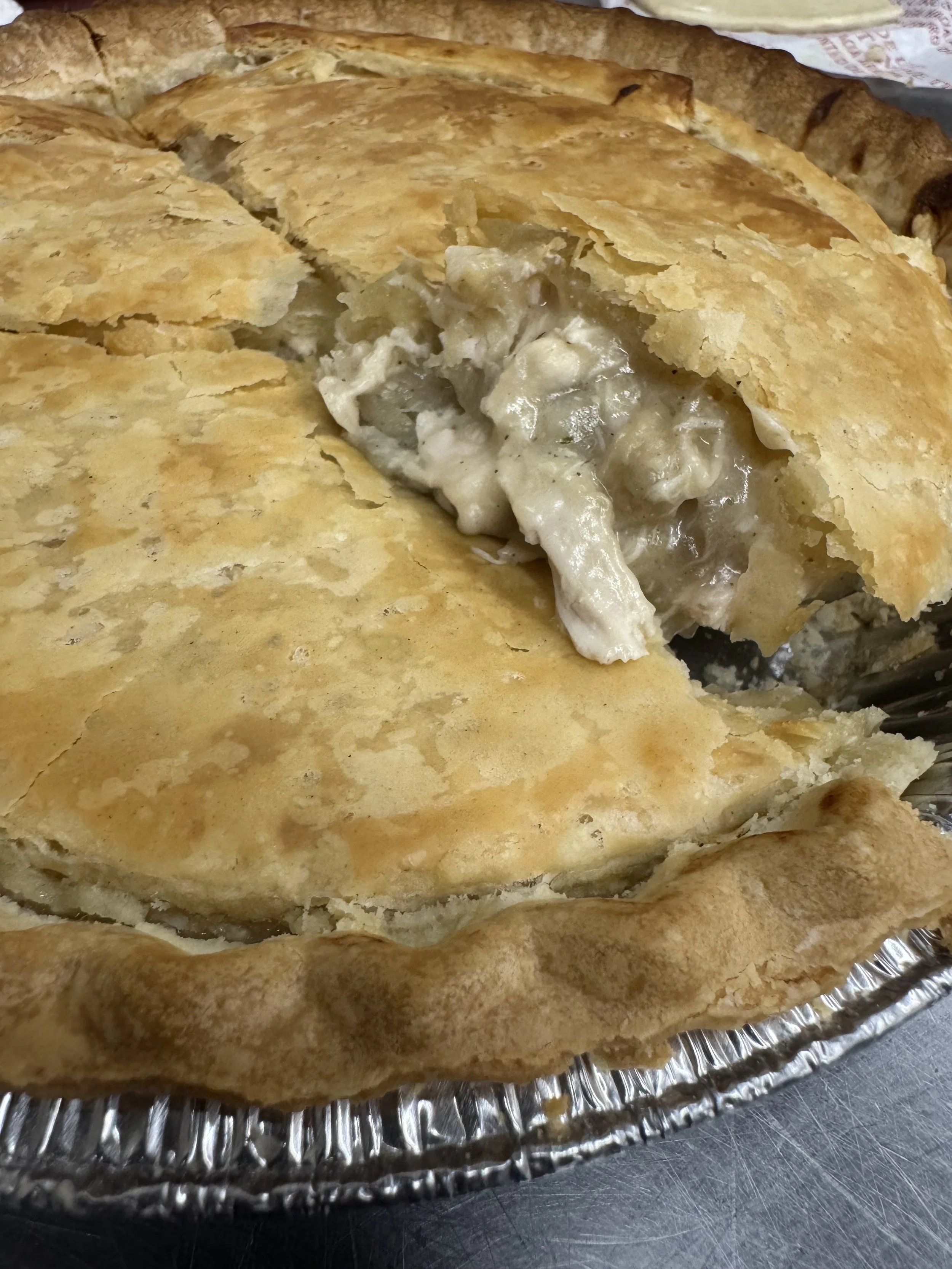 A freshly baked chicken pot pie in a foil pie plate with a golden crust, partially cut to reveal chicken and vegetable filling inside.
