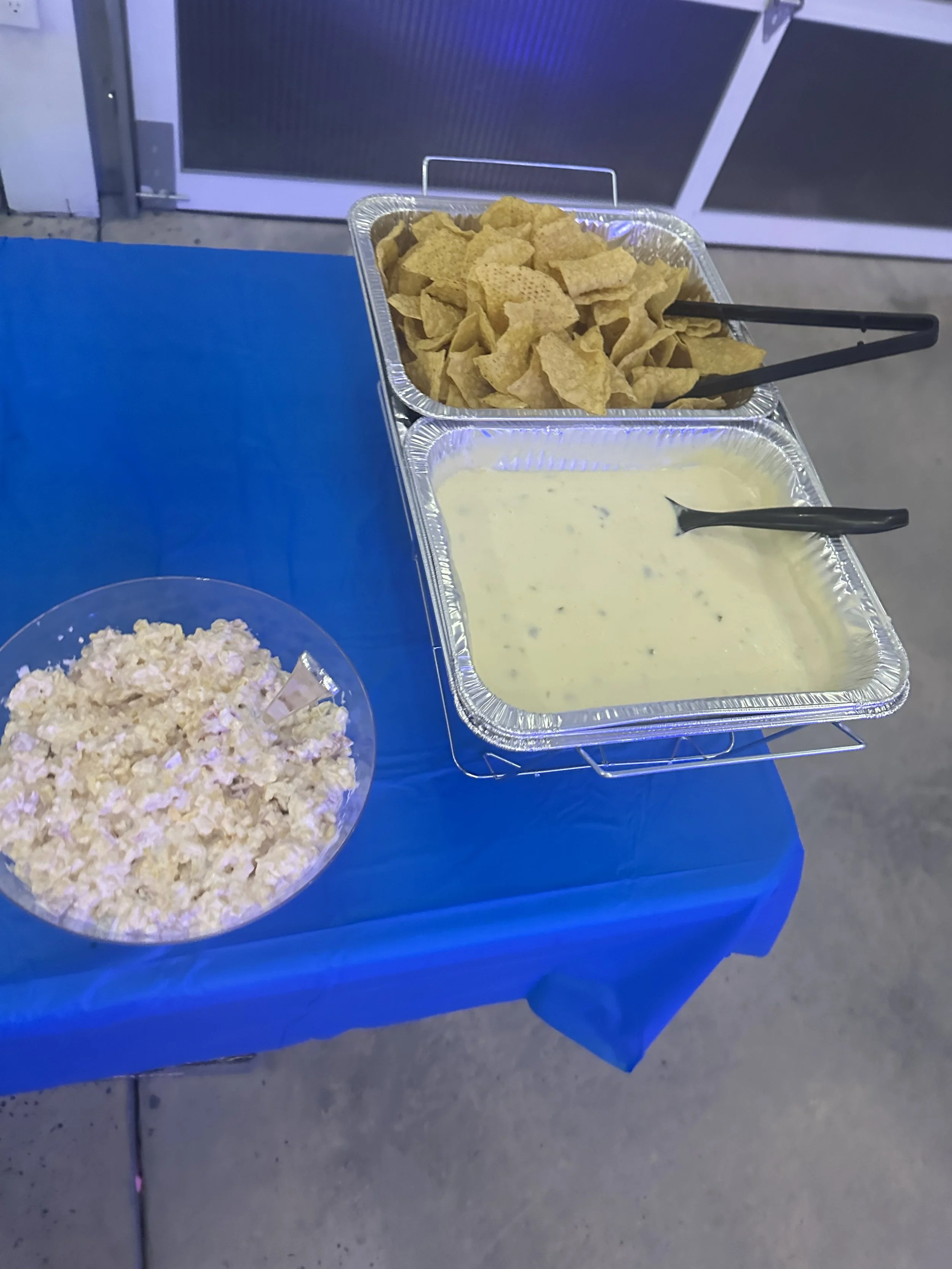 Buffet table with potato chips, ranch dip, and popcorn on a blue tablecloth.