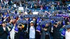 A large group of Seattle Reign FC fans at Lumen Field are standing up, holding their scarves above their heads. The scarves say "Seattle Reign FC"