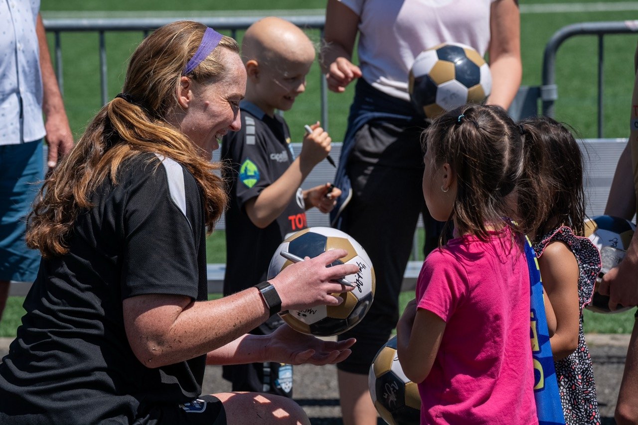 Cassie Miller signing a soccer ball for children