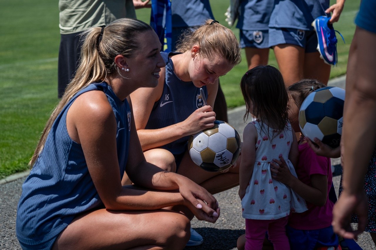 Reign FC players signing soccer balls for children