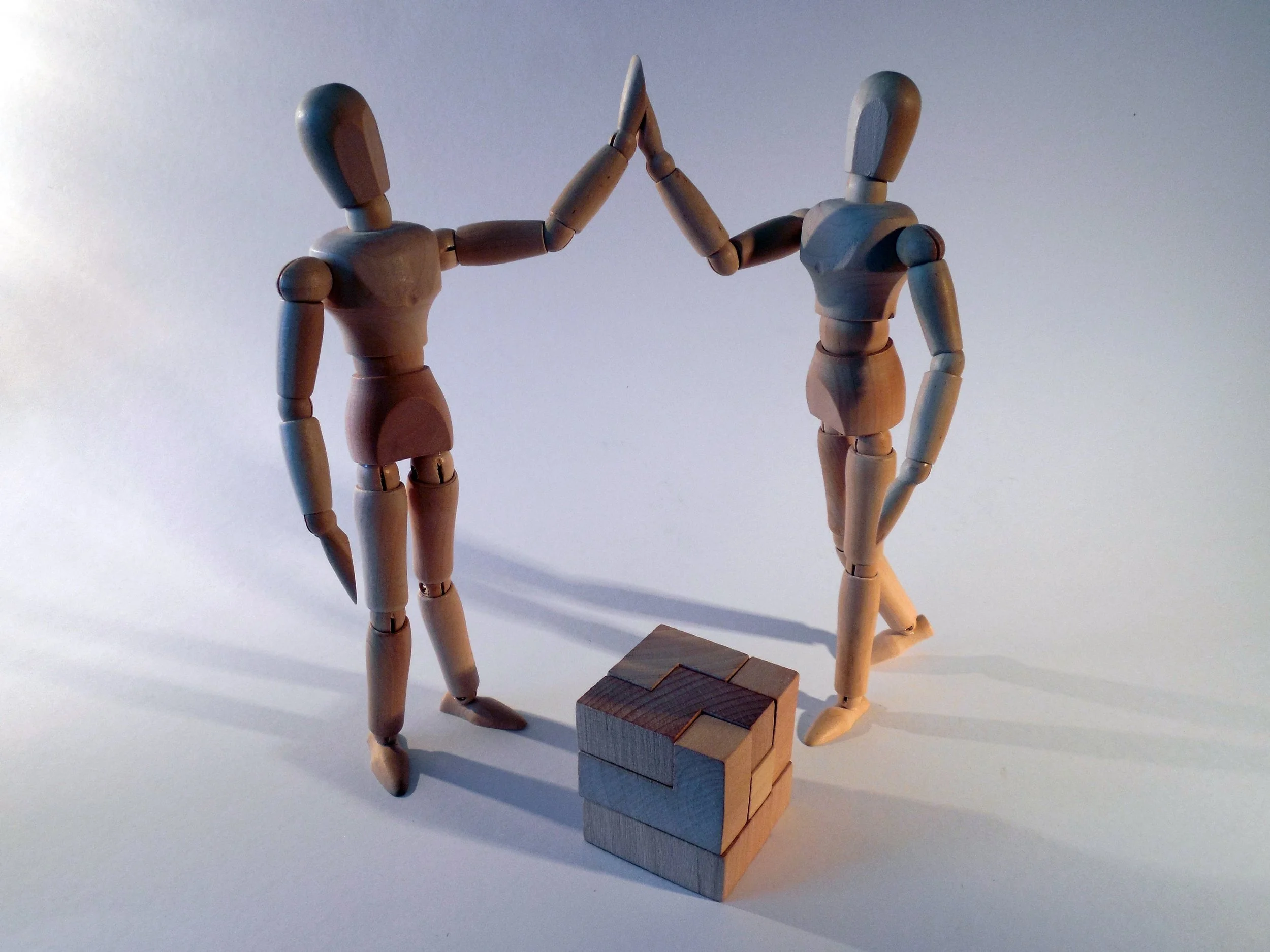 Two wooden statuettes high-fiving over the completion of a wooden block puzzle