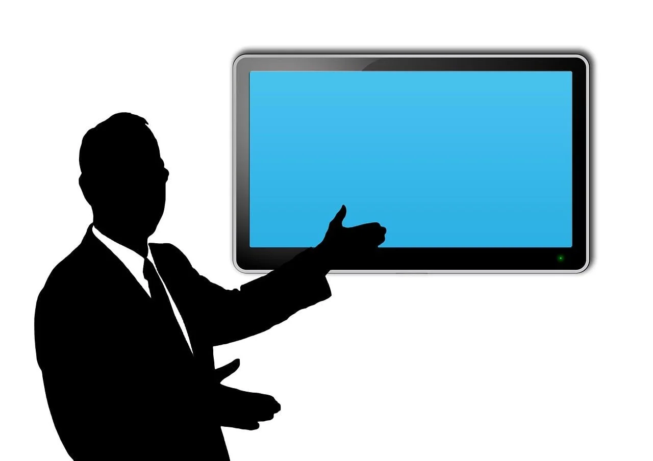 Silhouette of man gesturing towards computer screen.