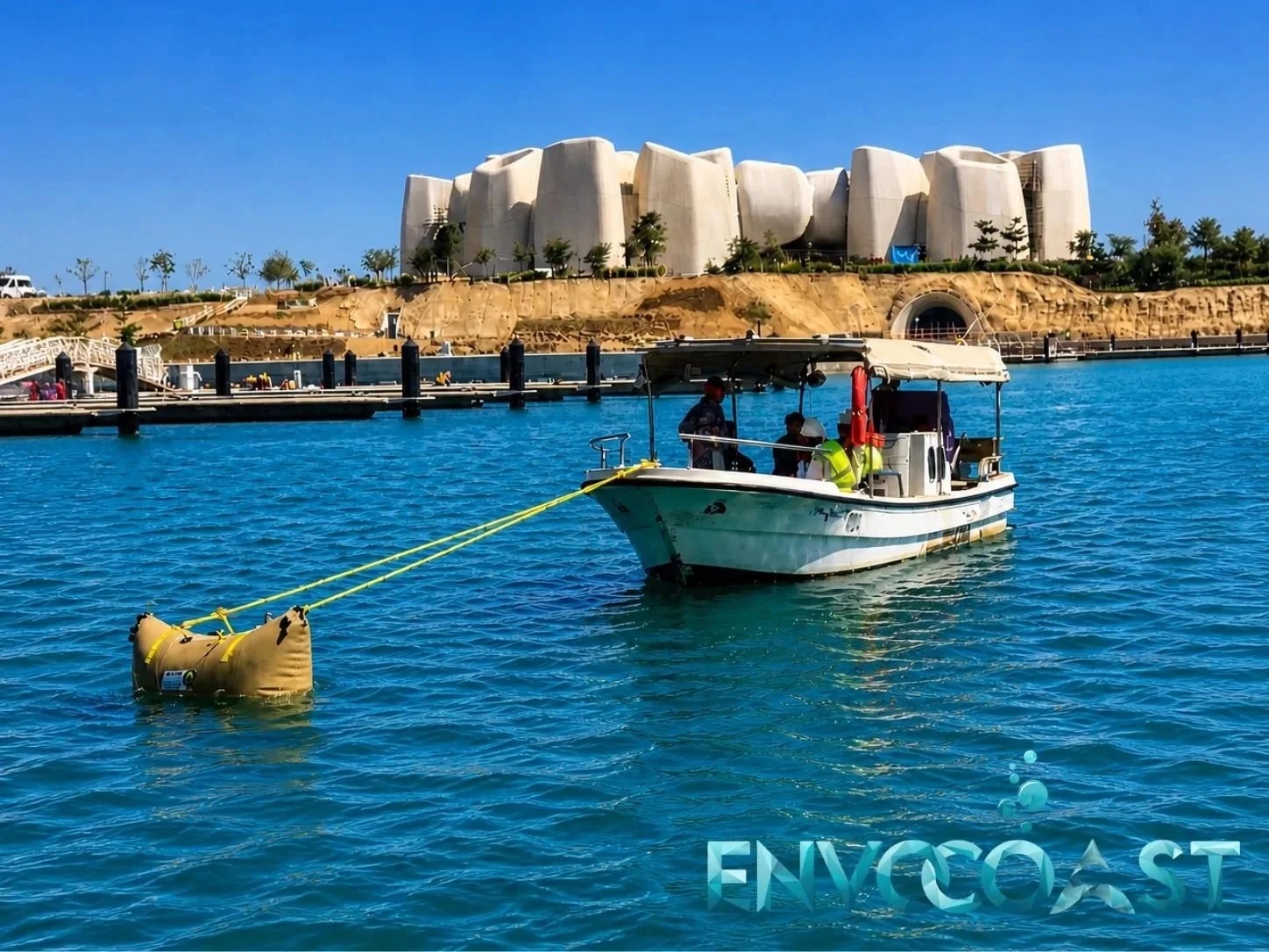 Workers on a small boat installing a yellow containment boom from Envocoast in KSA