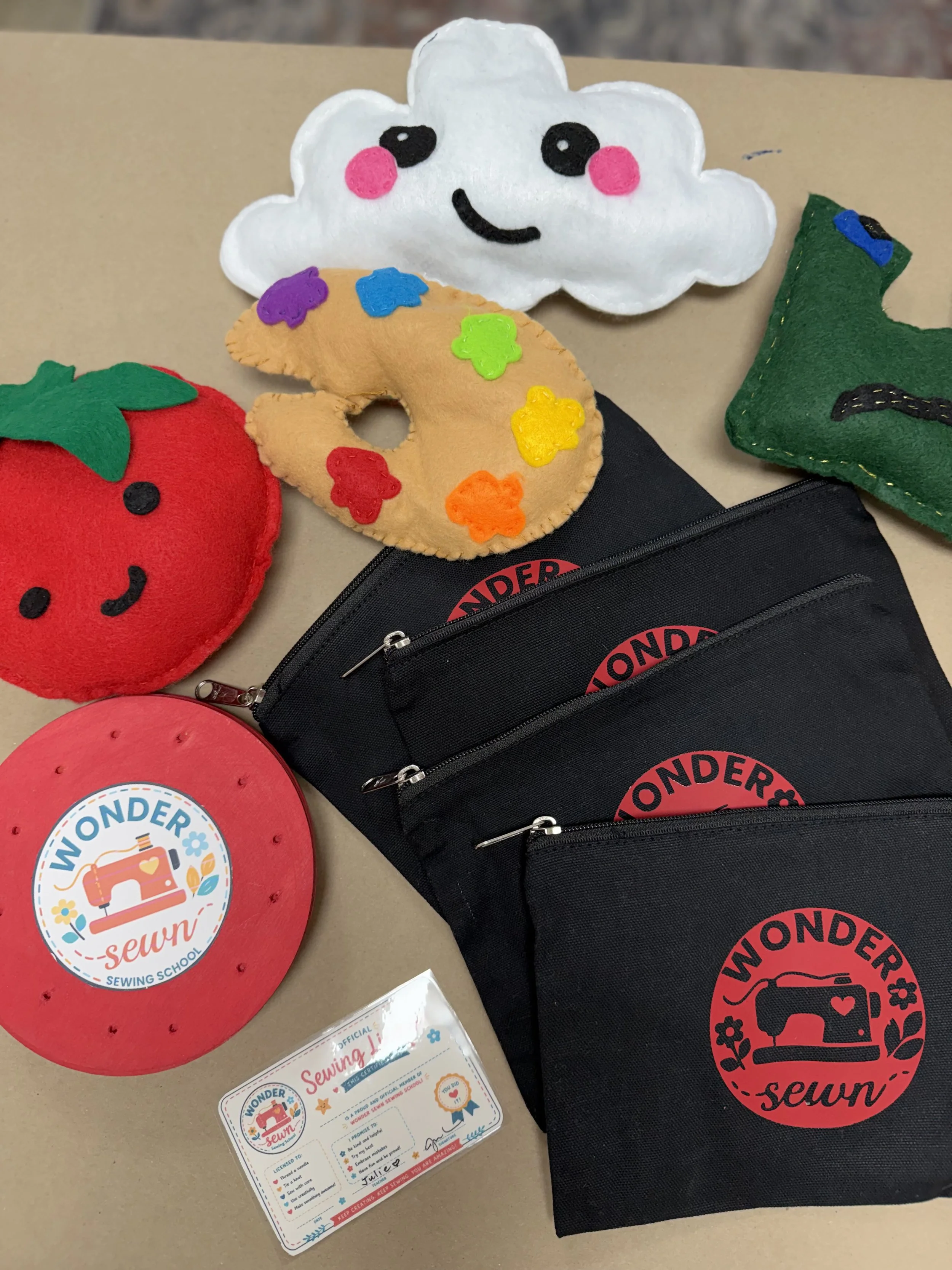 A collection of sewing-related items, including felt plush toys of a smiling cloud, a strawberry, and a green Christmas tree, along with a black pouch, a sewing badge, and a certificate of completion from a sewing school.