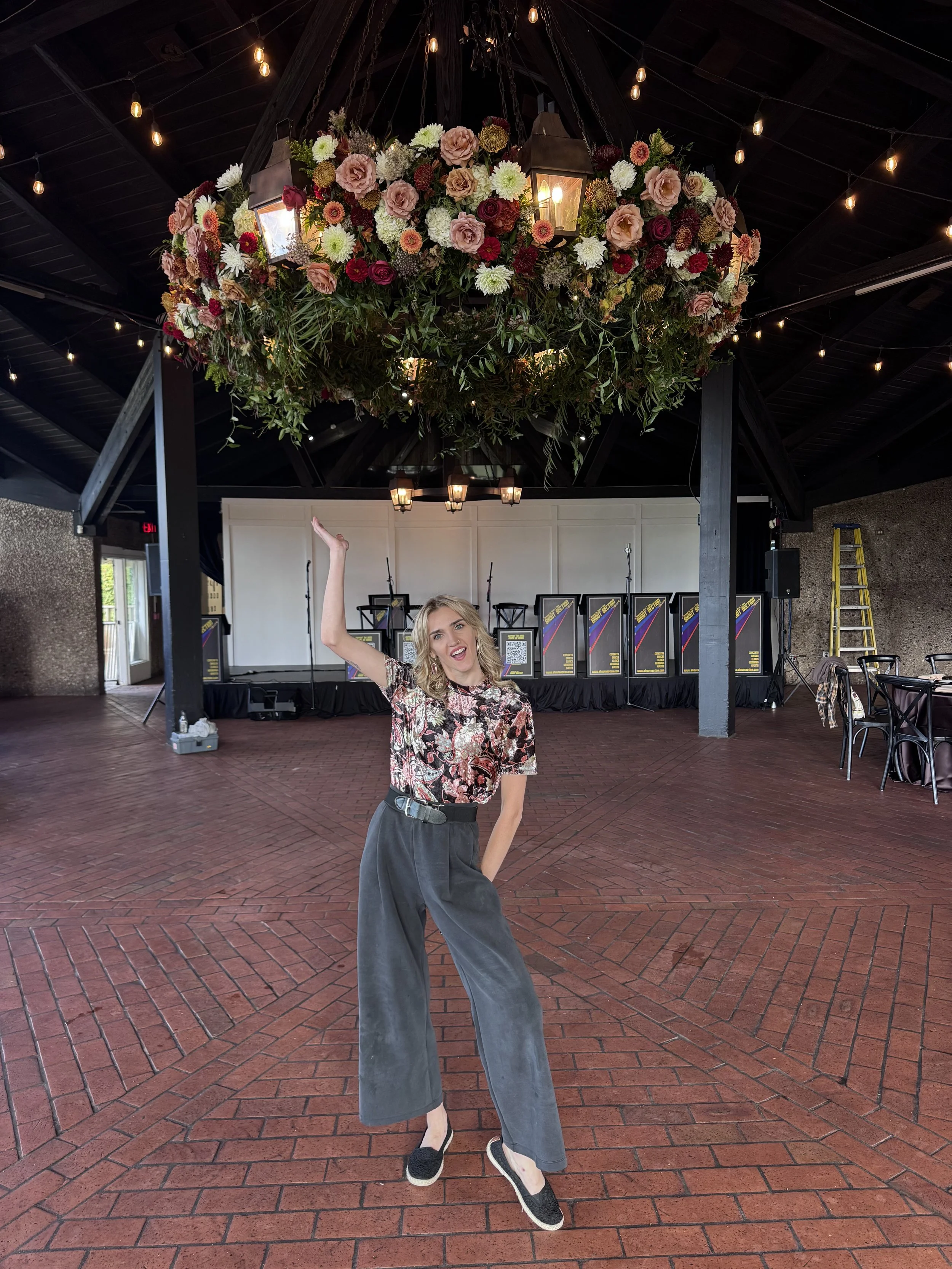 A woman dancing at an indoor event space with a large floral chandelier hanging from the ceiling.