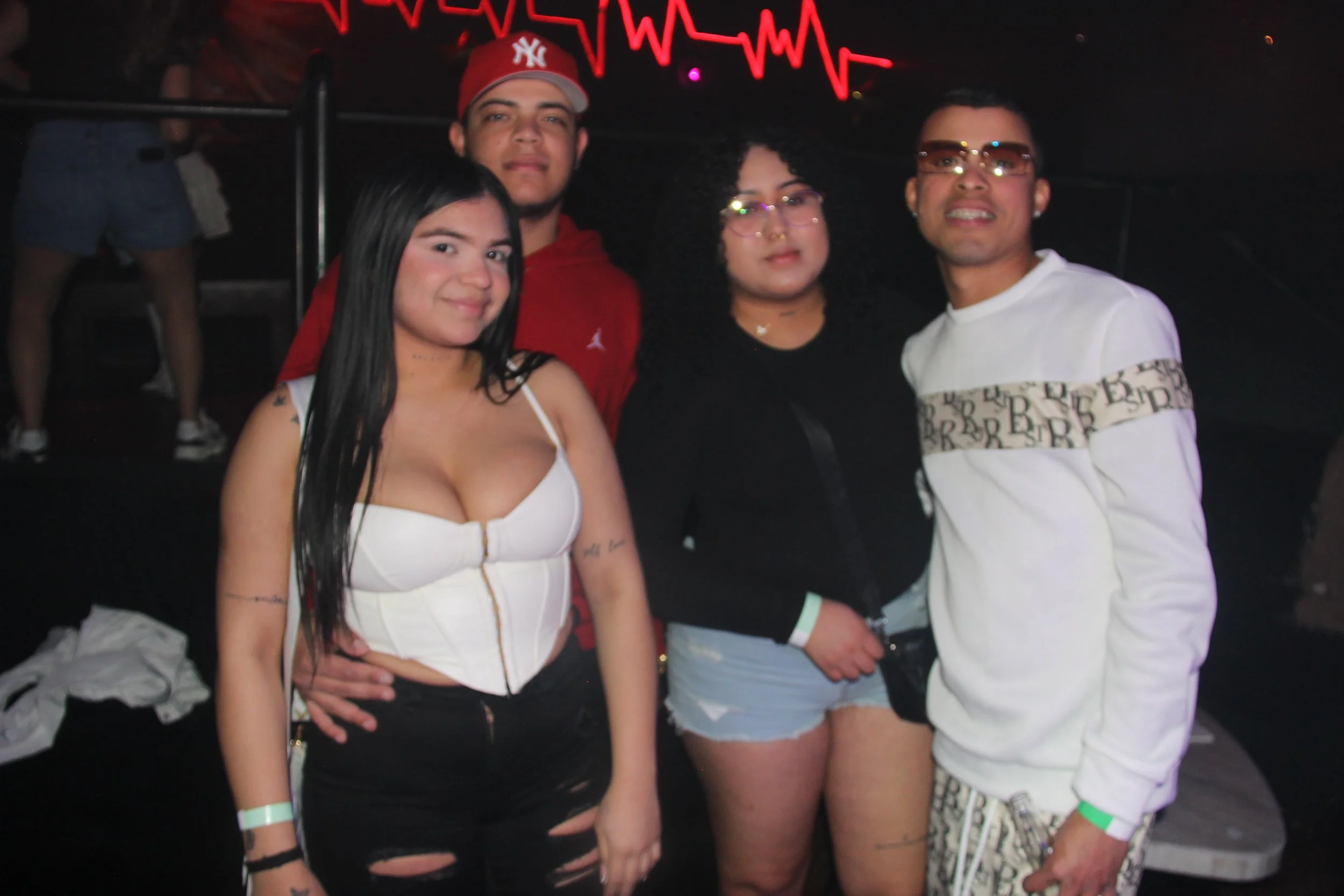 Four young adults posing together in a club with neon lights in the background.