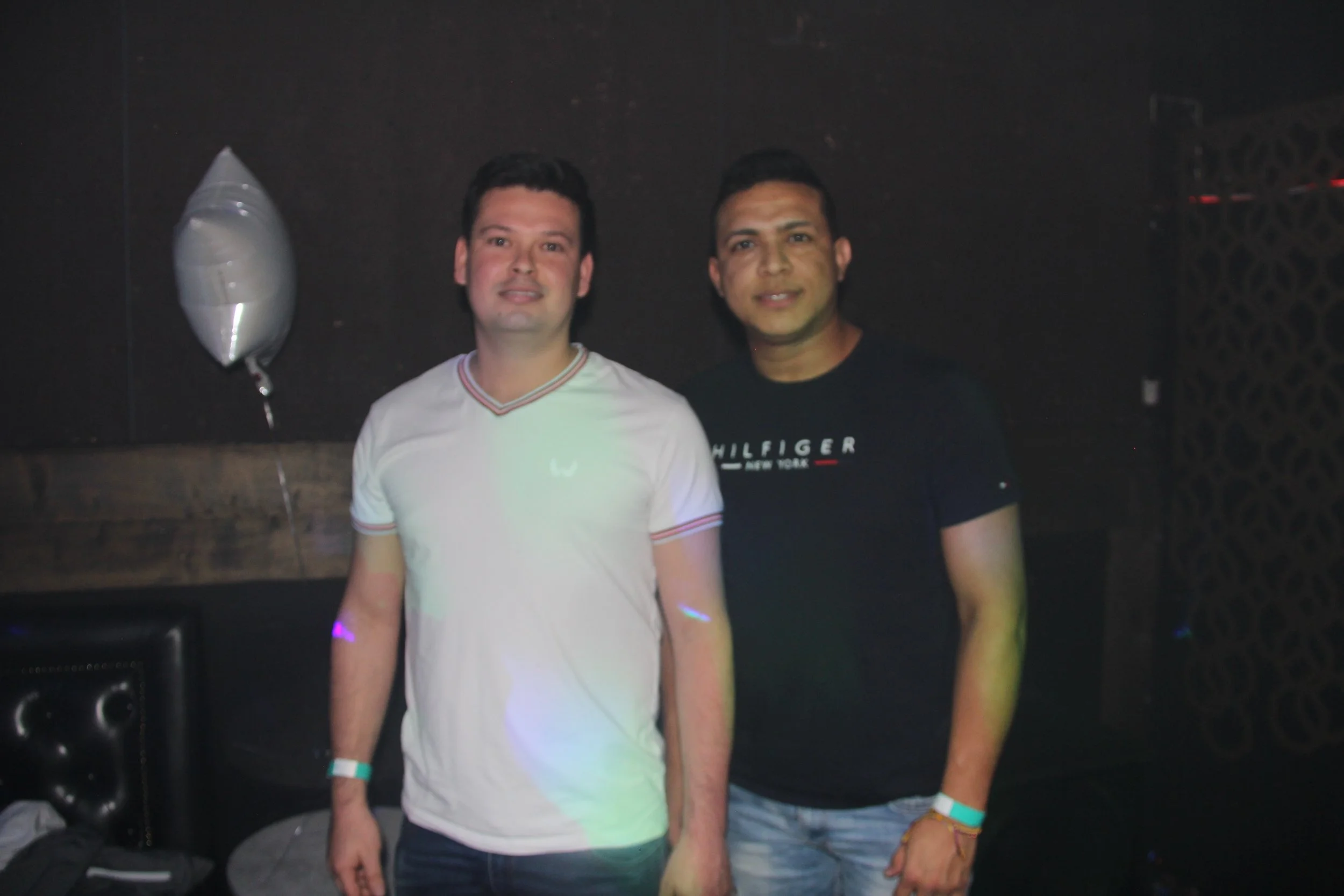 Two men standing together in a dimly lit room with a white balloon nearby.