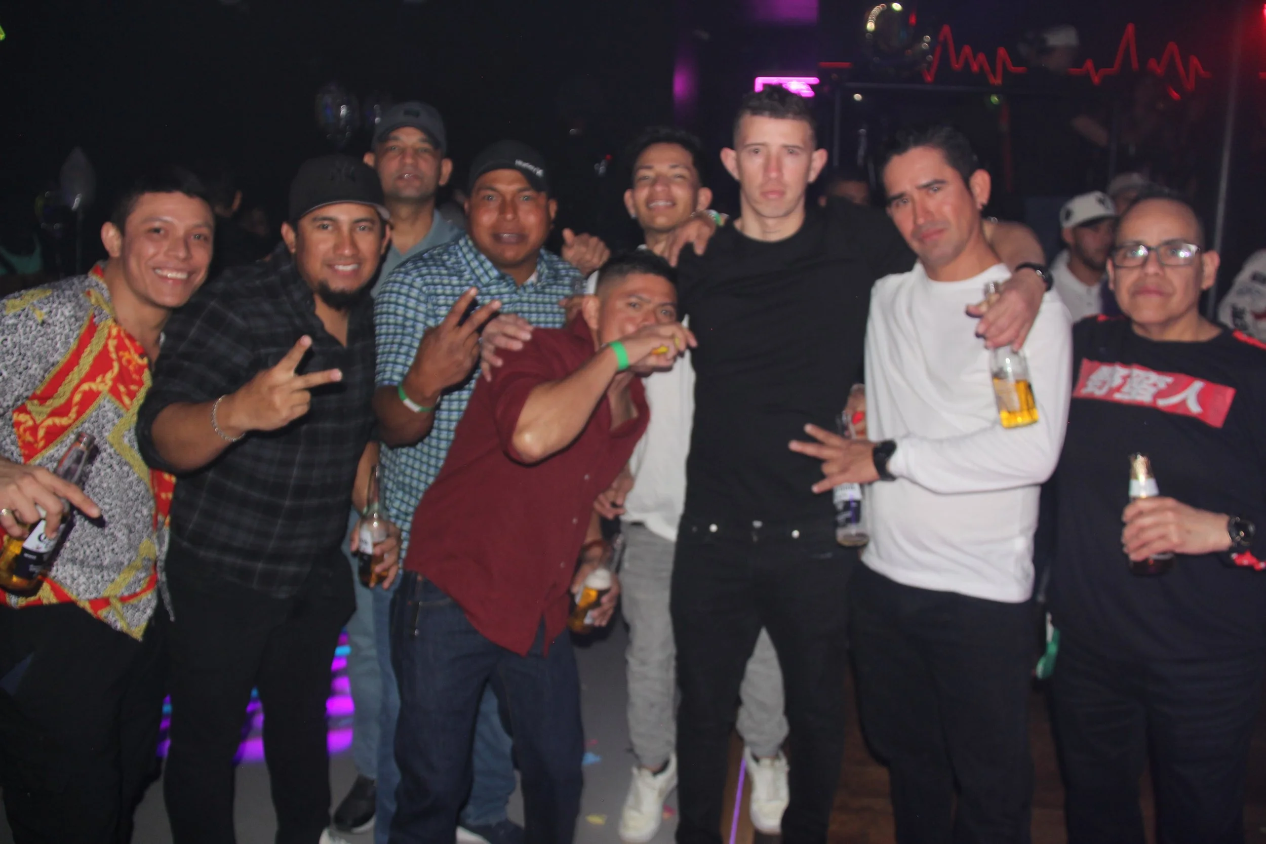 Group of men posing at a nightclub with drinks, colorful lights in the background.