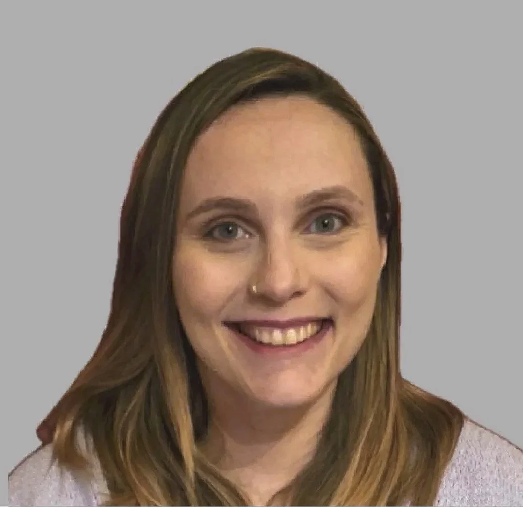 A woman smiling with shoulder-length brown hair, wearing a light-colored top, against a plain gray background.