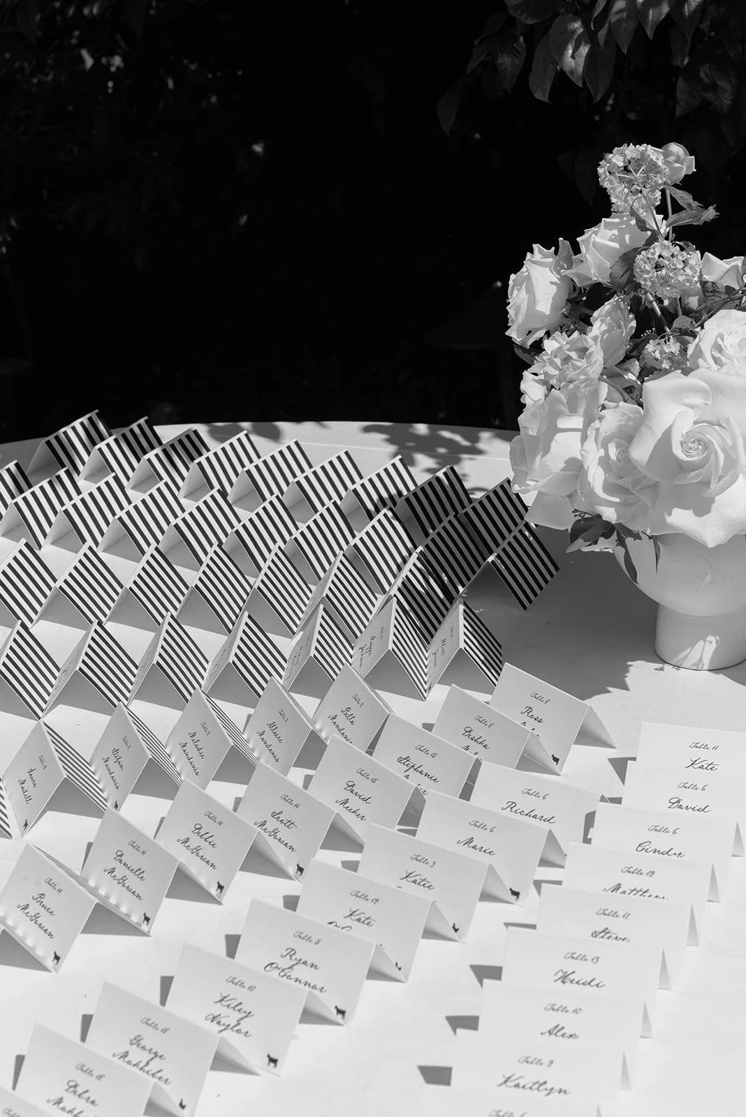 Black-and-white overhead photograph of striped escort cards arranged beside white wedding flowers at Goodstone Inn.