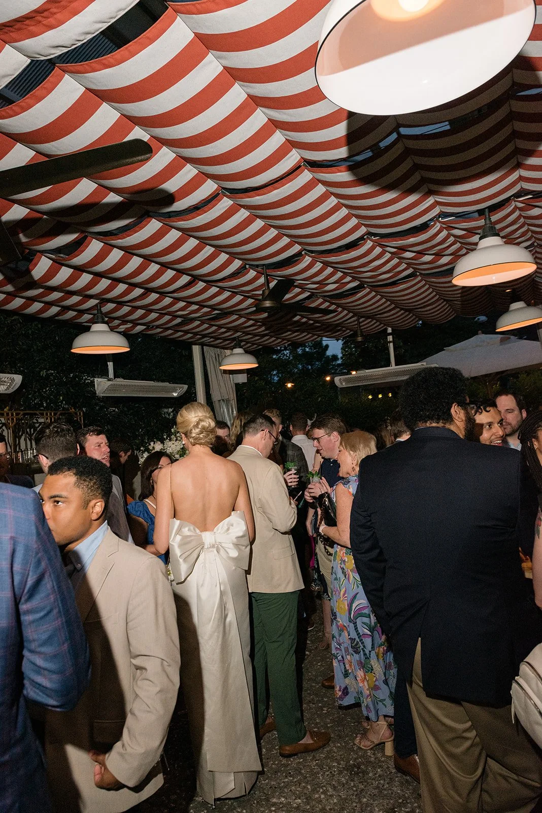 Wedding guests gather outdoors beneath red and white striped awnings during cocktail hour at a coastal destination celebration.