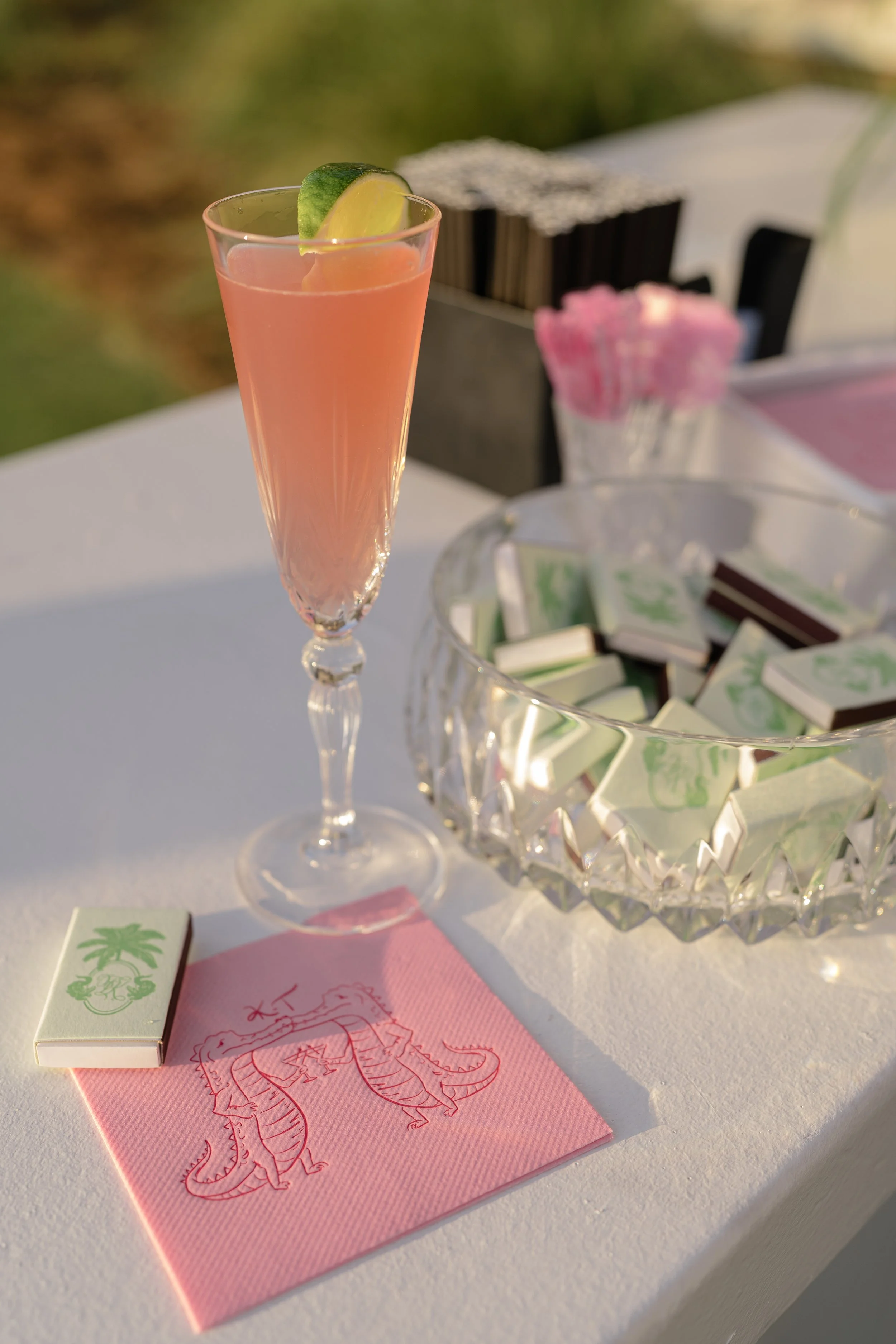 Pink signature cocktail with citrus garnish displayed beside custom monogrammed cocktail napkins.