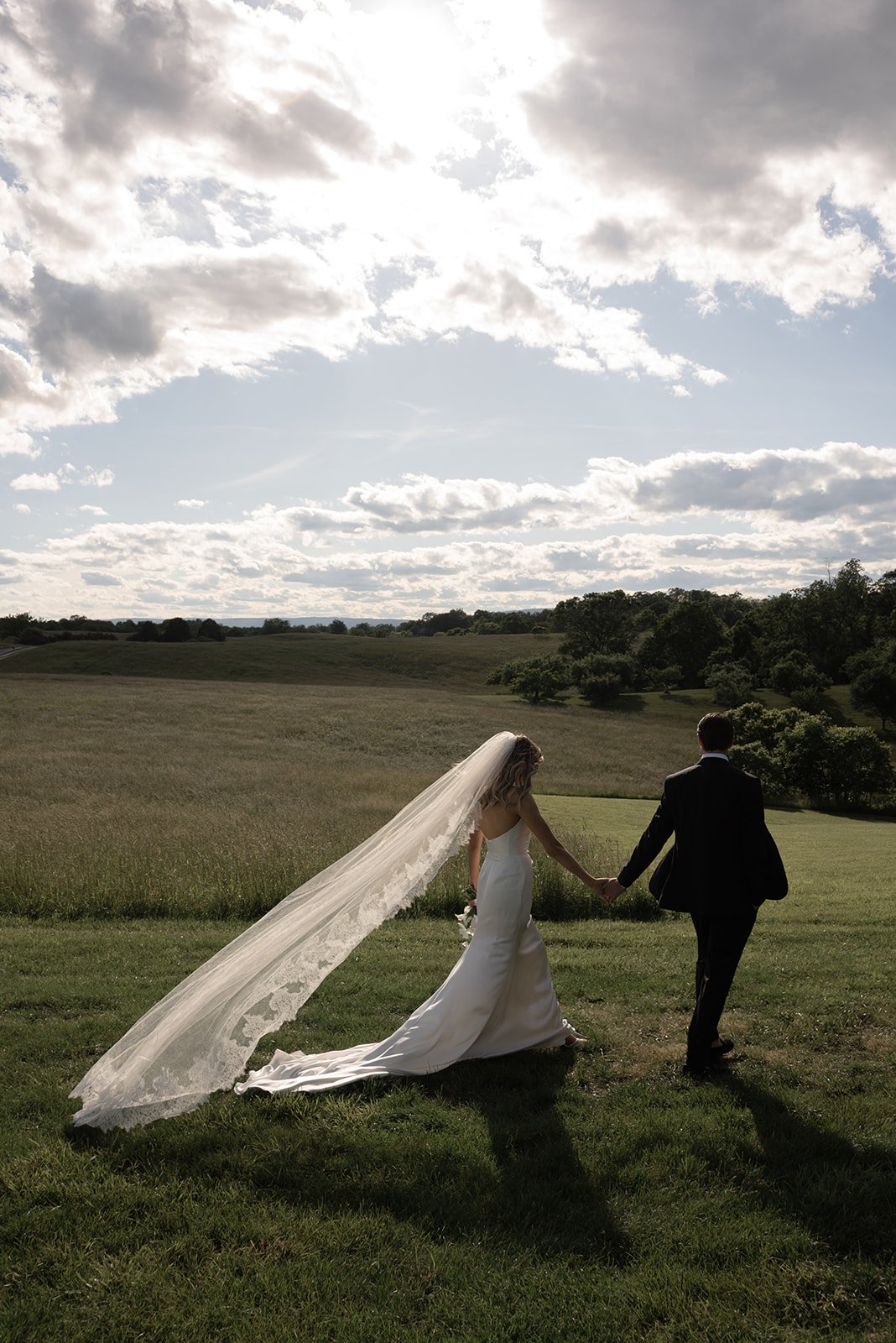 Bride and groom walking into the open Hayfield at Goodstone Inn beneath a bright spring sky.