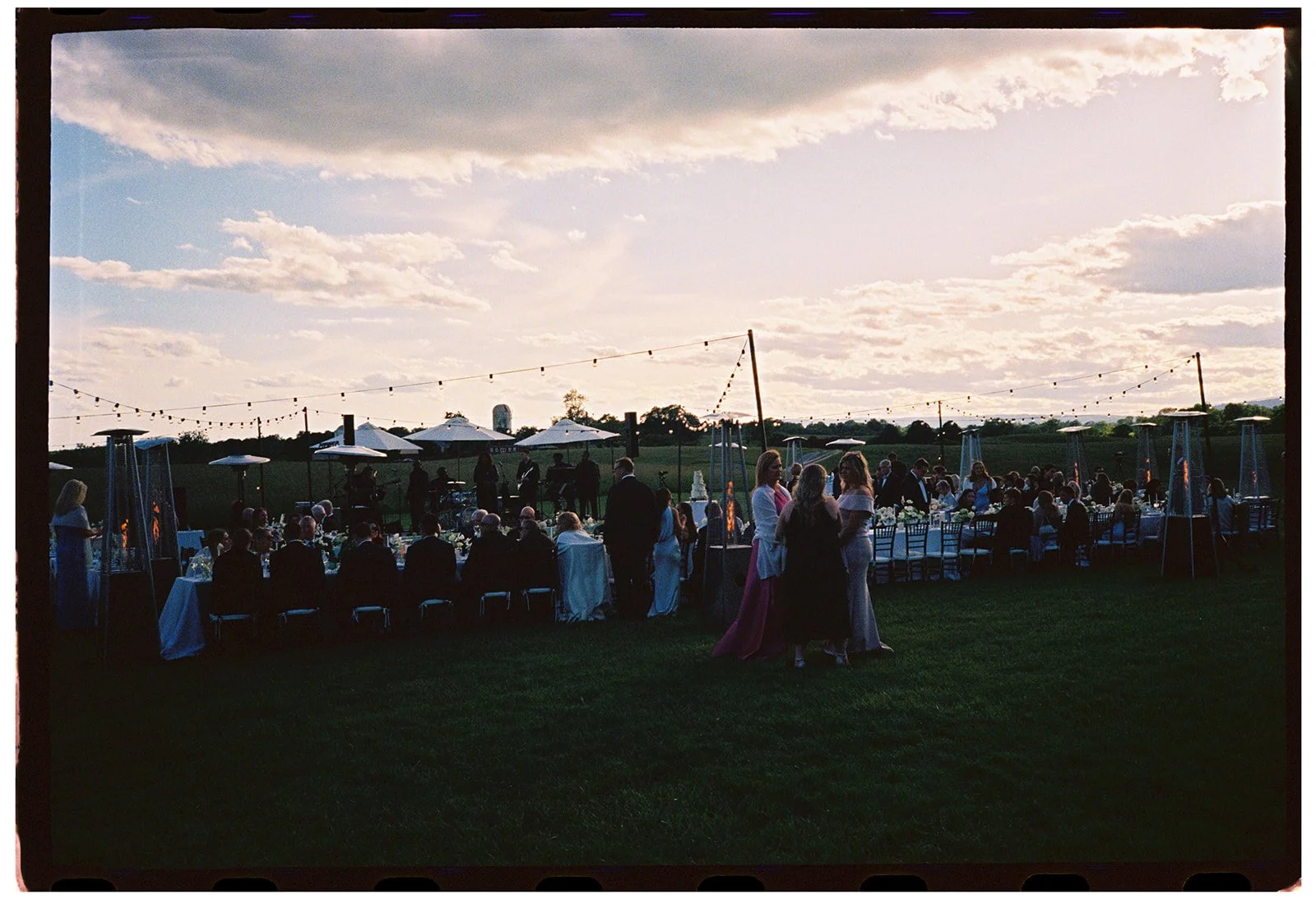 Wide view film photo of guests seated at long dinner tables during sunset at Goodstone Inn.