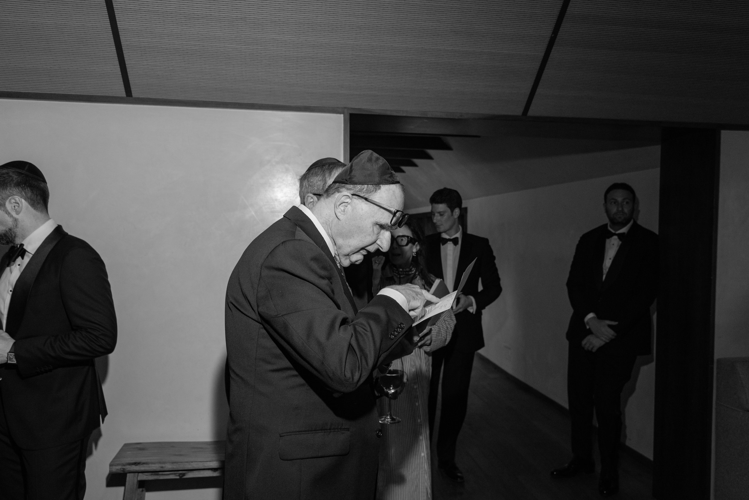 A documentary black and white photo of the Rabbi studying his paperwork with his glasses pushed up on his forehead in the foyer of Blue Hill. 