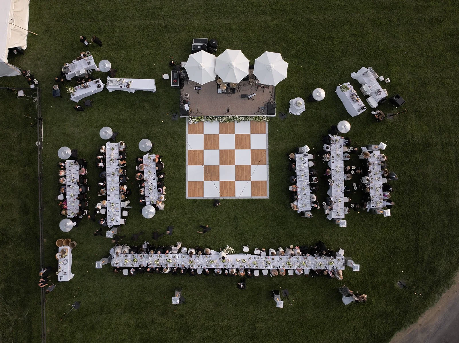Aerial drone view of long reception tables and a checkerboard dance floor arranged in the Hayfield at Goodstone Inn.