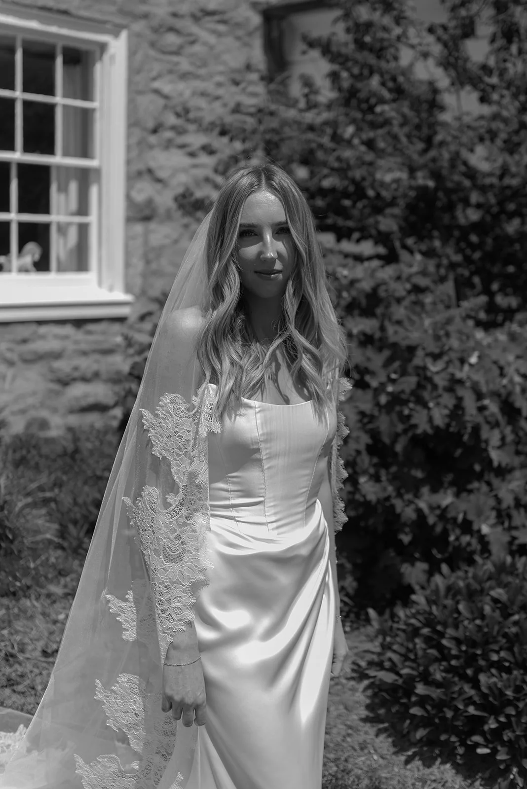 Black-and-white portrait of the bride walking with her veil trailing beside the Manor House at Goodstone Inn.