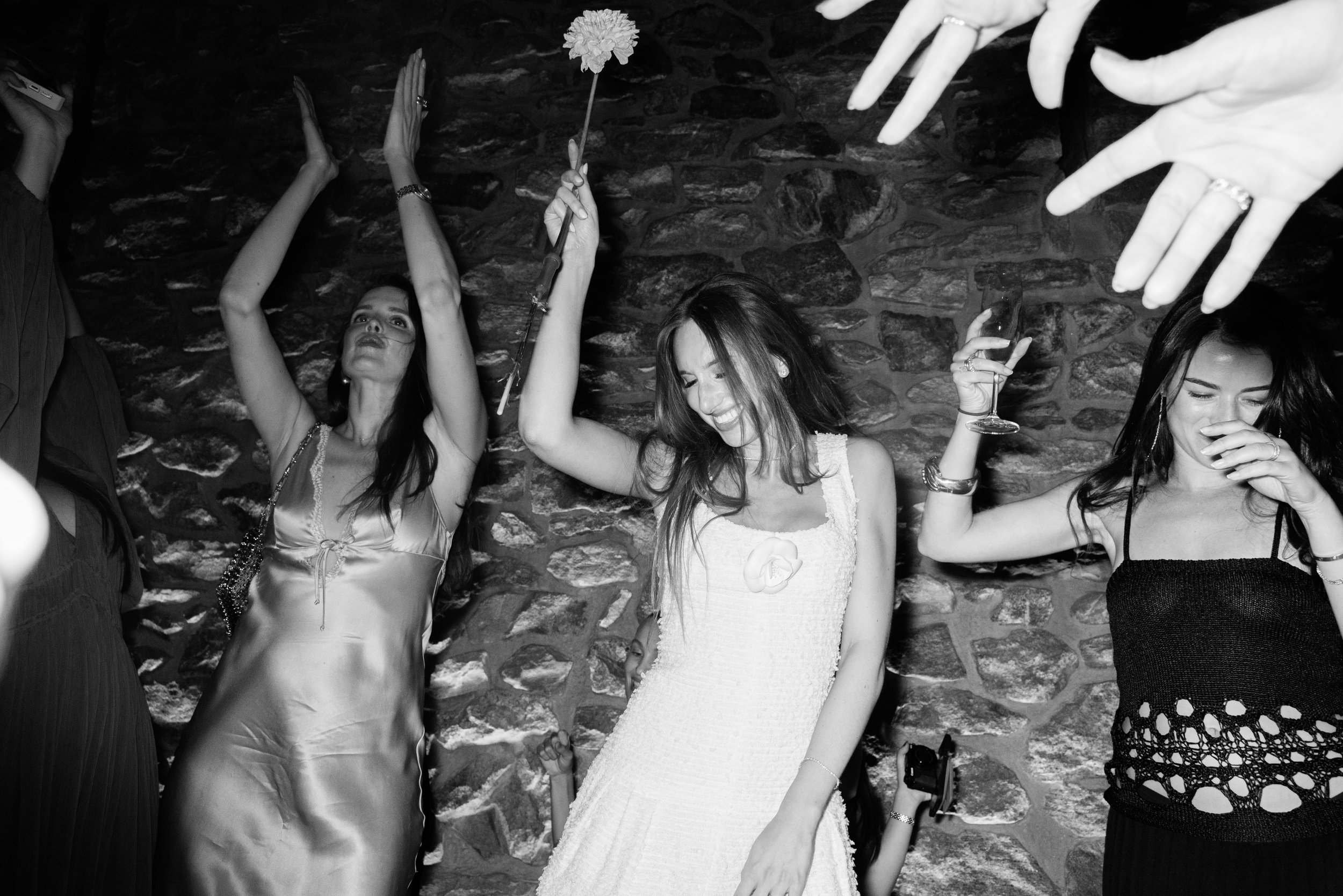 Black-and-white reception photograph of Jennie and guests dancing beneath raised hands on the tables inside the dining hall at Blue Hill. 