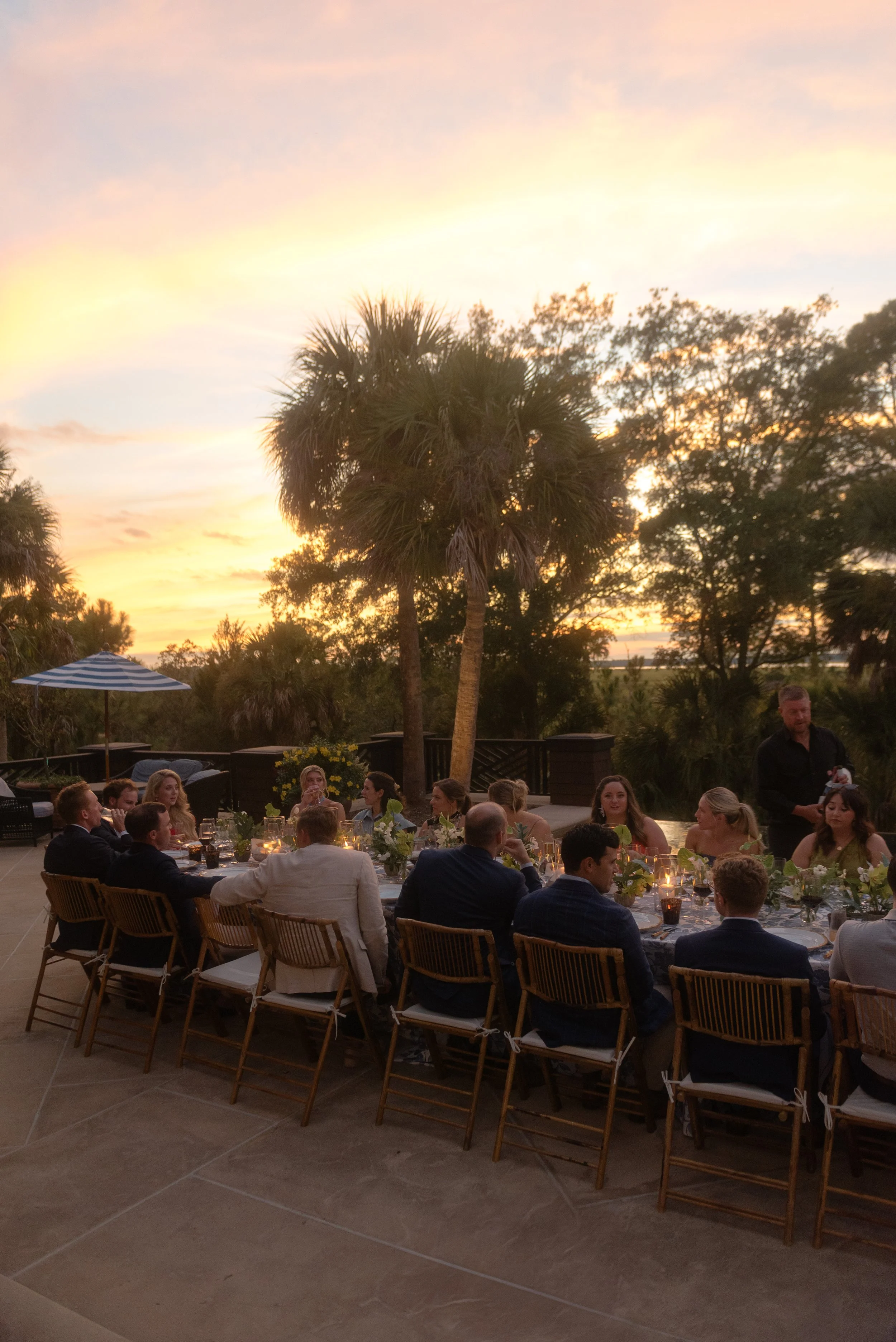 Family and friends gather around candlelit tables at sunset during a rehearsal dinner at a private Kiawah Island estate.
