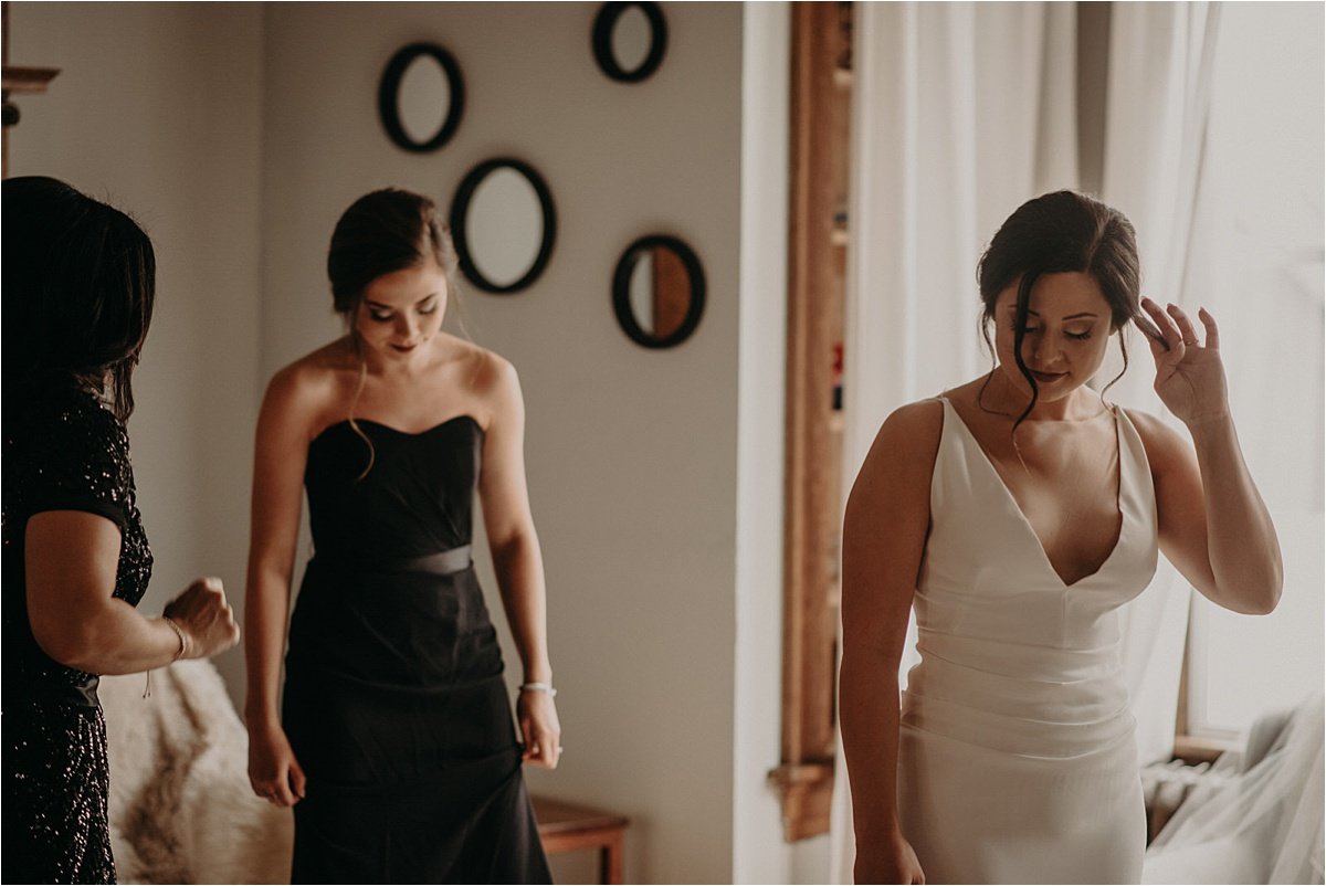 The bride's mother and sister helps her dress in her wedding gown