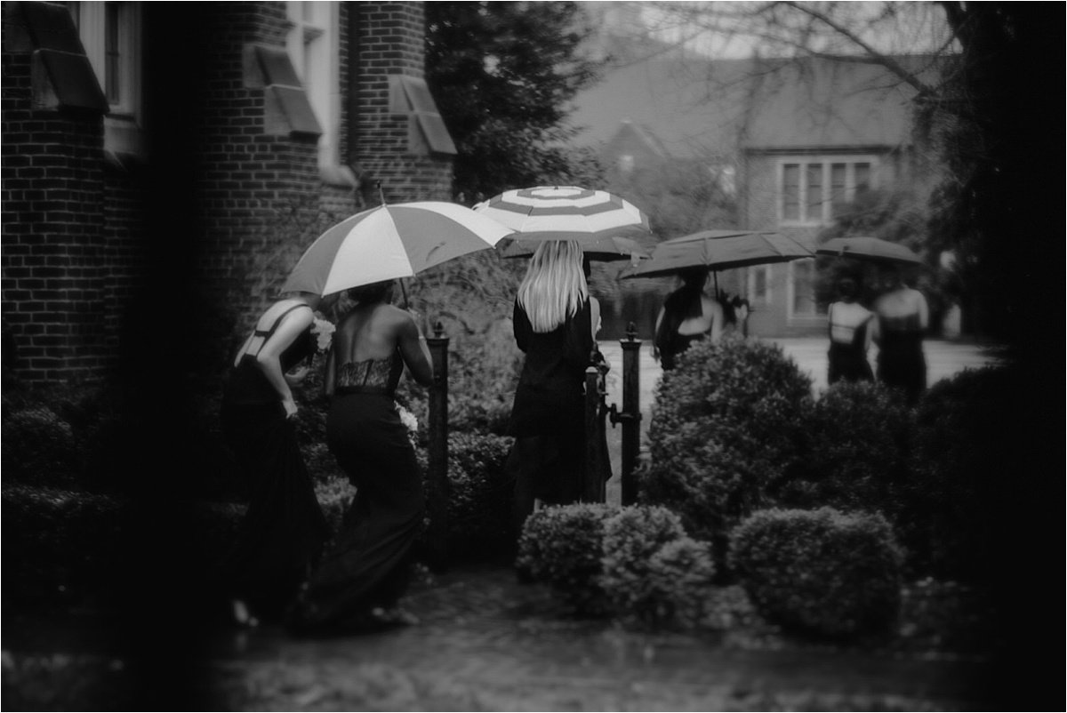 The wedding party heads to the ceremony under the cover of umbrellas at this rainy winter wedding
