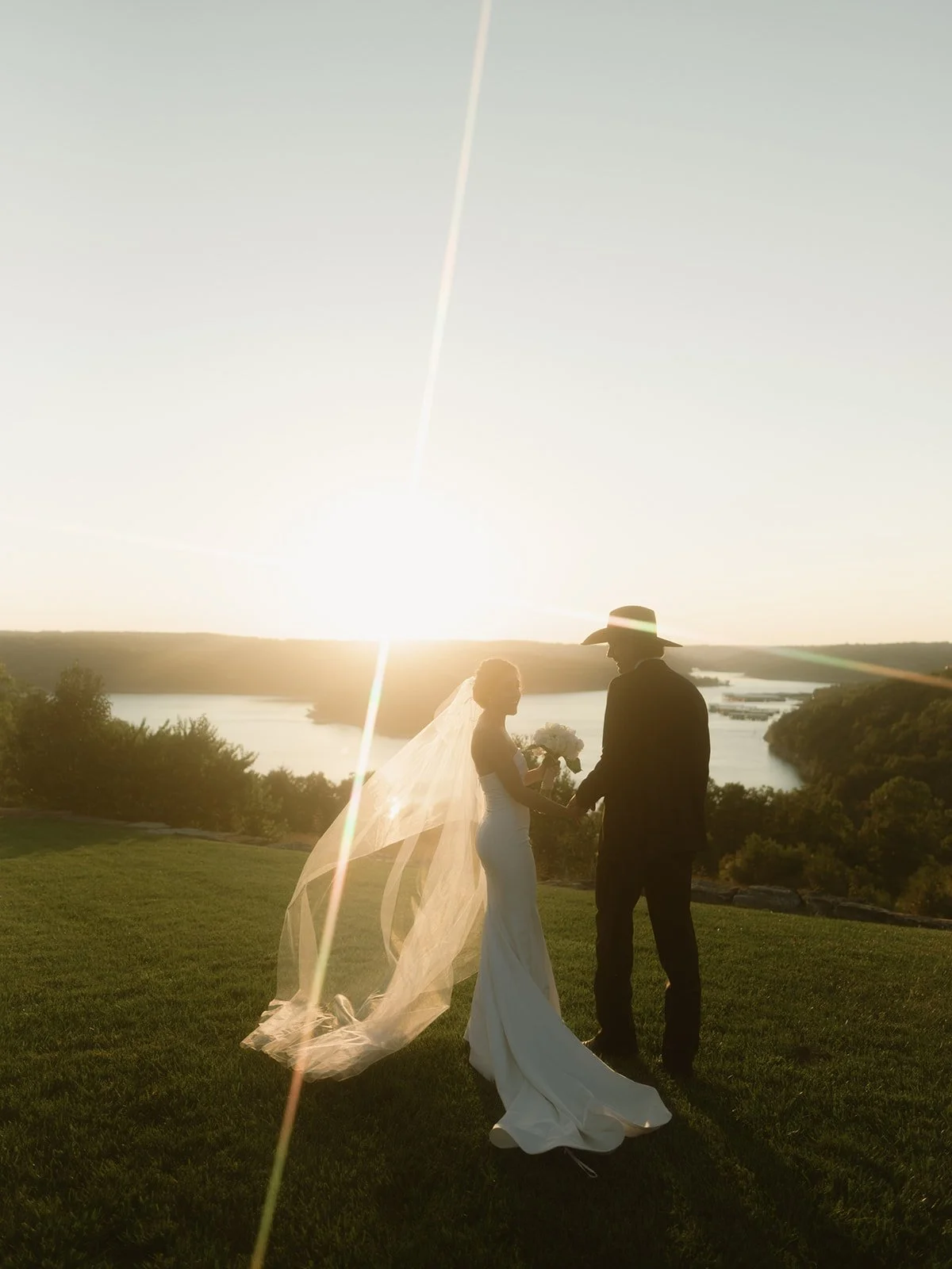 Bride and groom photographed in warm sunset light overlooking the Ozark lakes during their wedding weekend at the Integrity Hills Stables by Big Cedar Lodge in Ridgedale, Missouri.