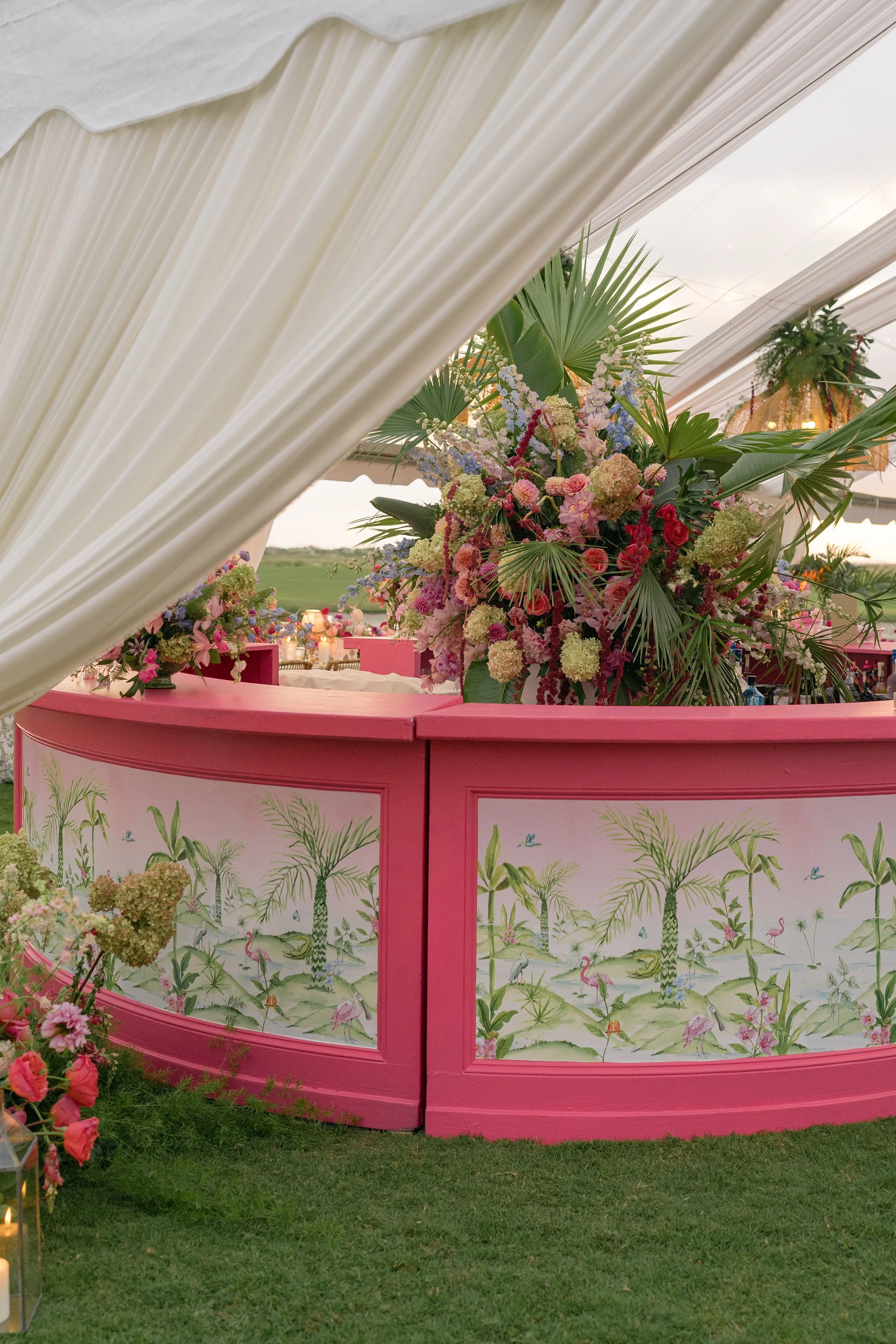 Custom pink reception bar with tropical illustrated panels and an abundant floral arrangement by Festoon.