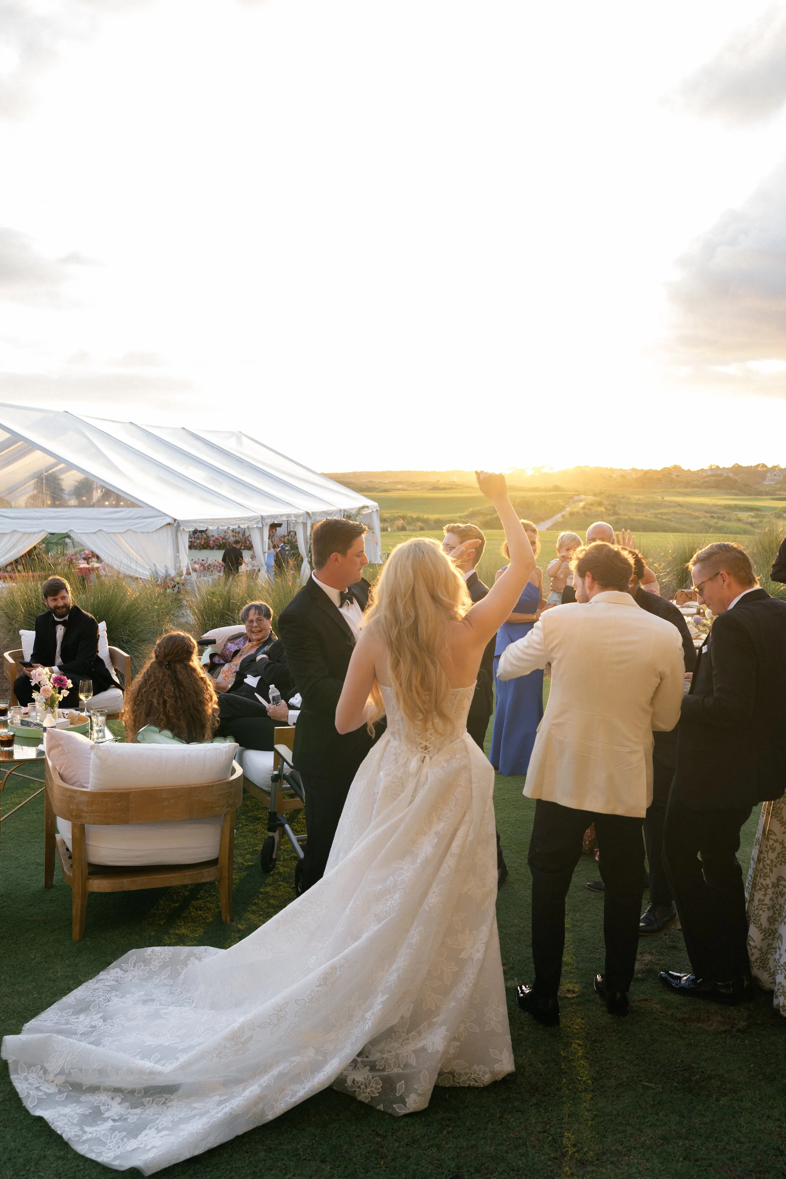 Katie walks toward guests gathered beneath the reception tent during golden-hour cocktail hour at The Ocean Course.