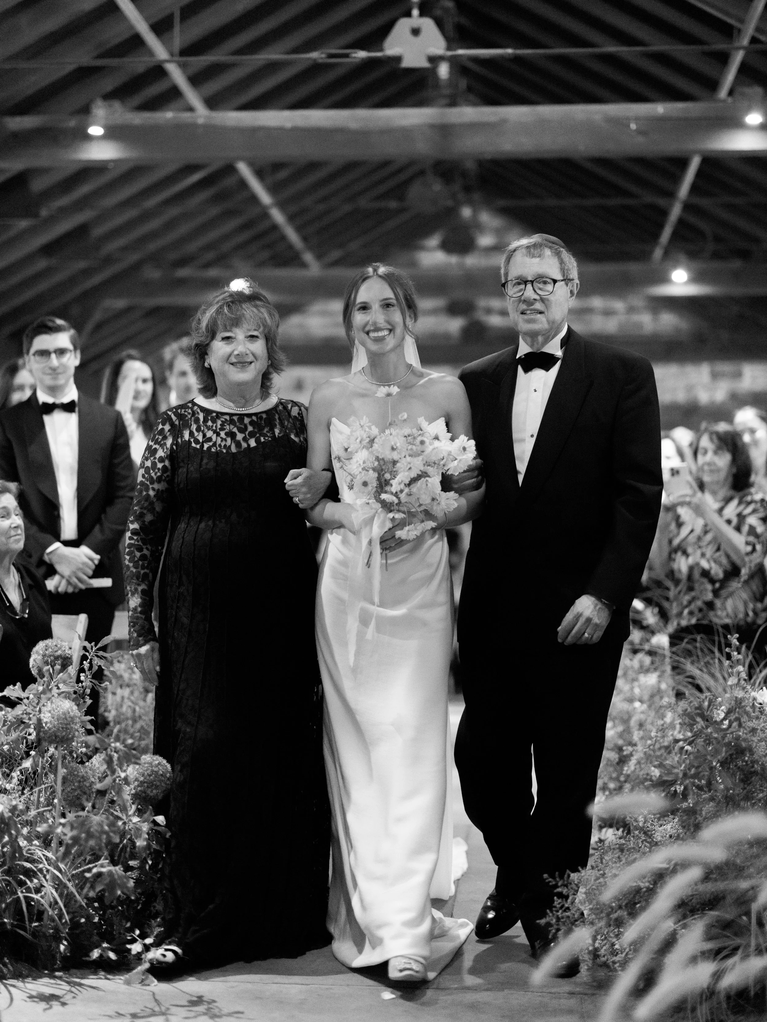 Bride entering her ceremony being escorted by both her mother and her father beneath the pergola at Blue Hill at Stone Barns.