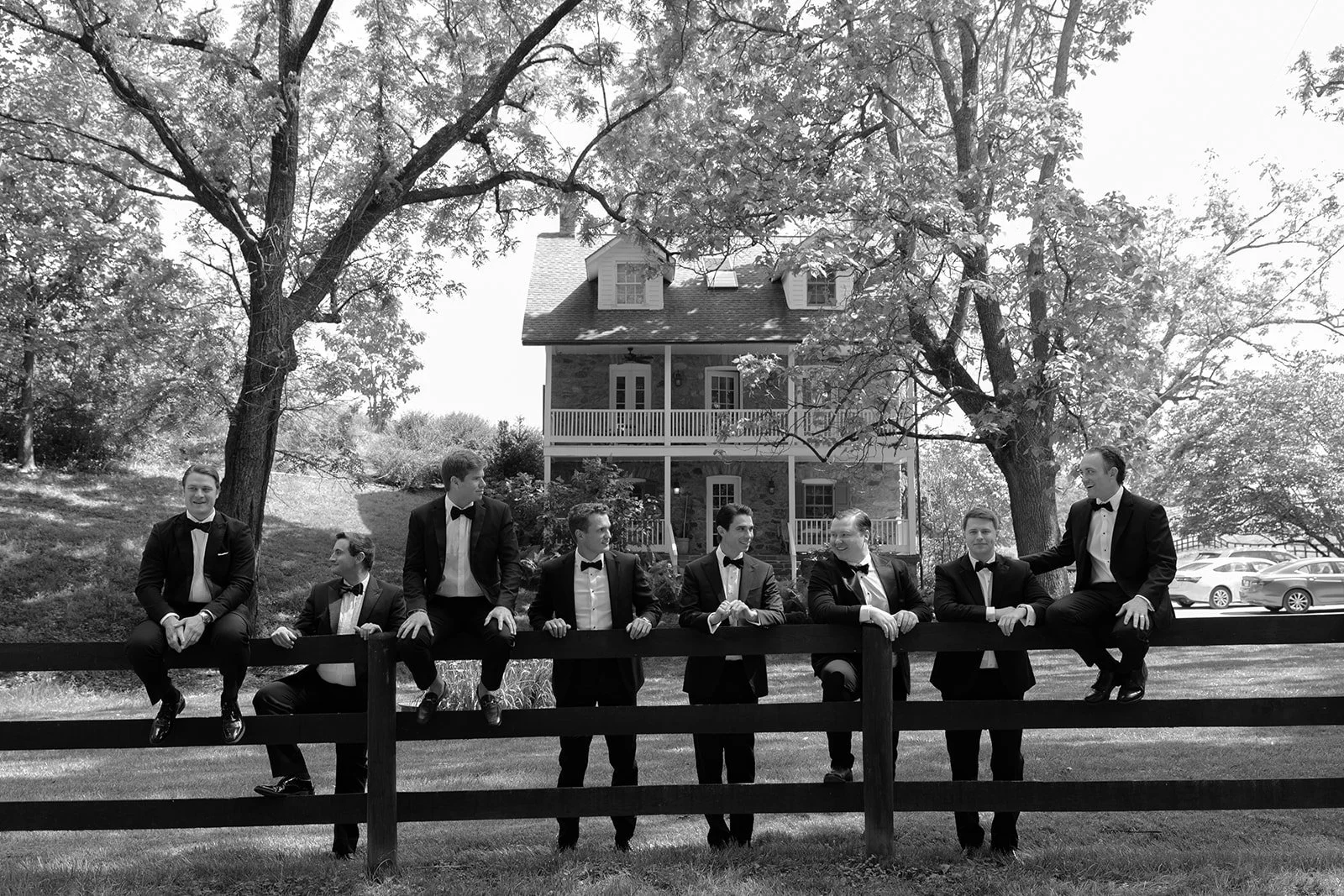 Black-and-white photograph of groomsmen gathered along a fence near the historic estate at Goodstone Inn.