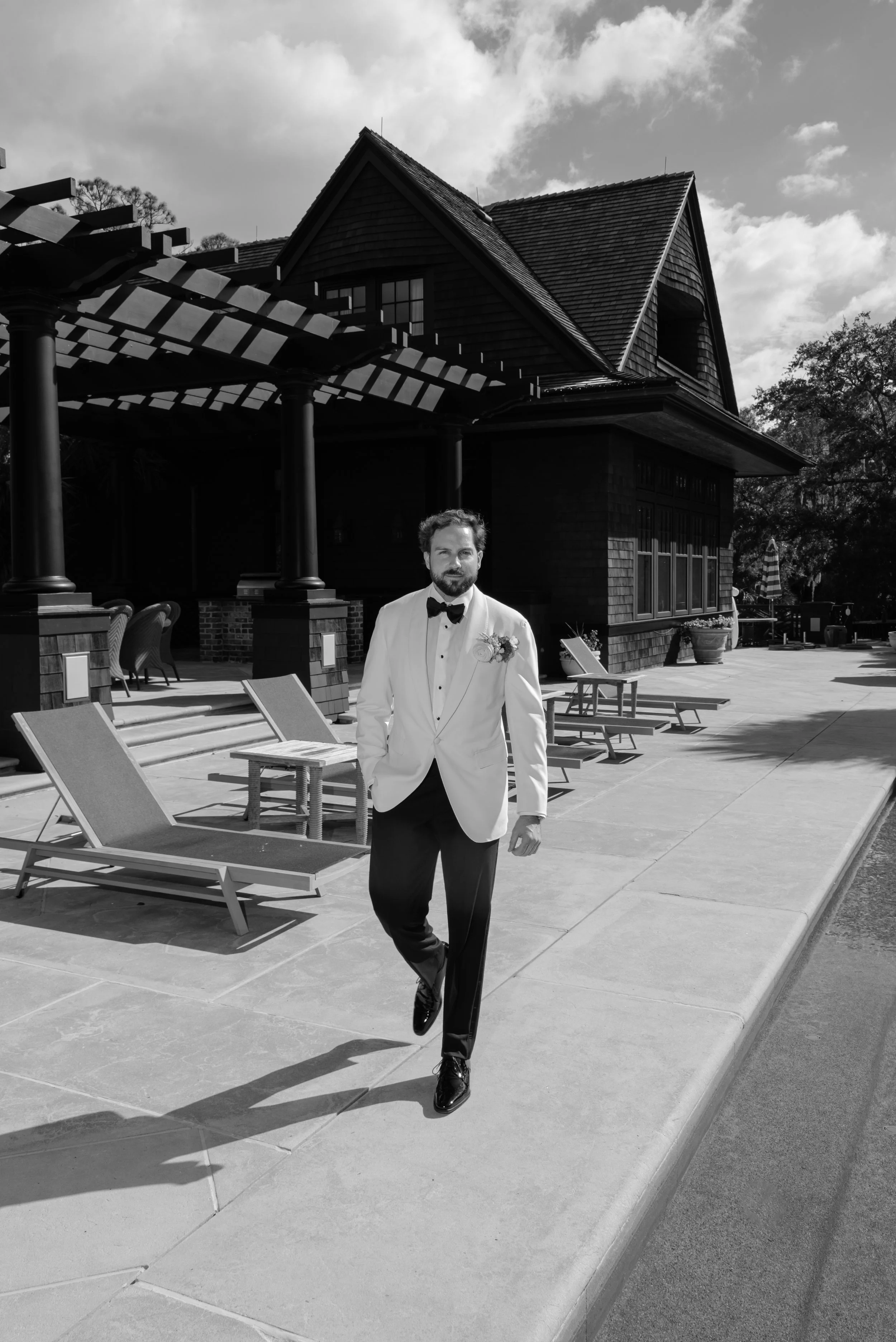 Black-and-white editorial portrait of the groom walking beside the private Kiawah Island estate in his white dinner jacket.