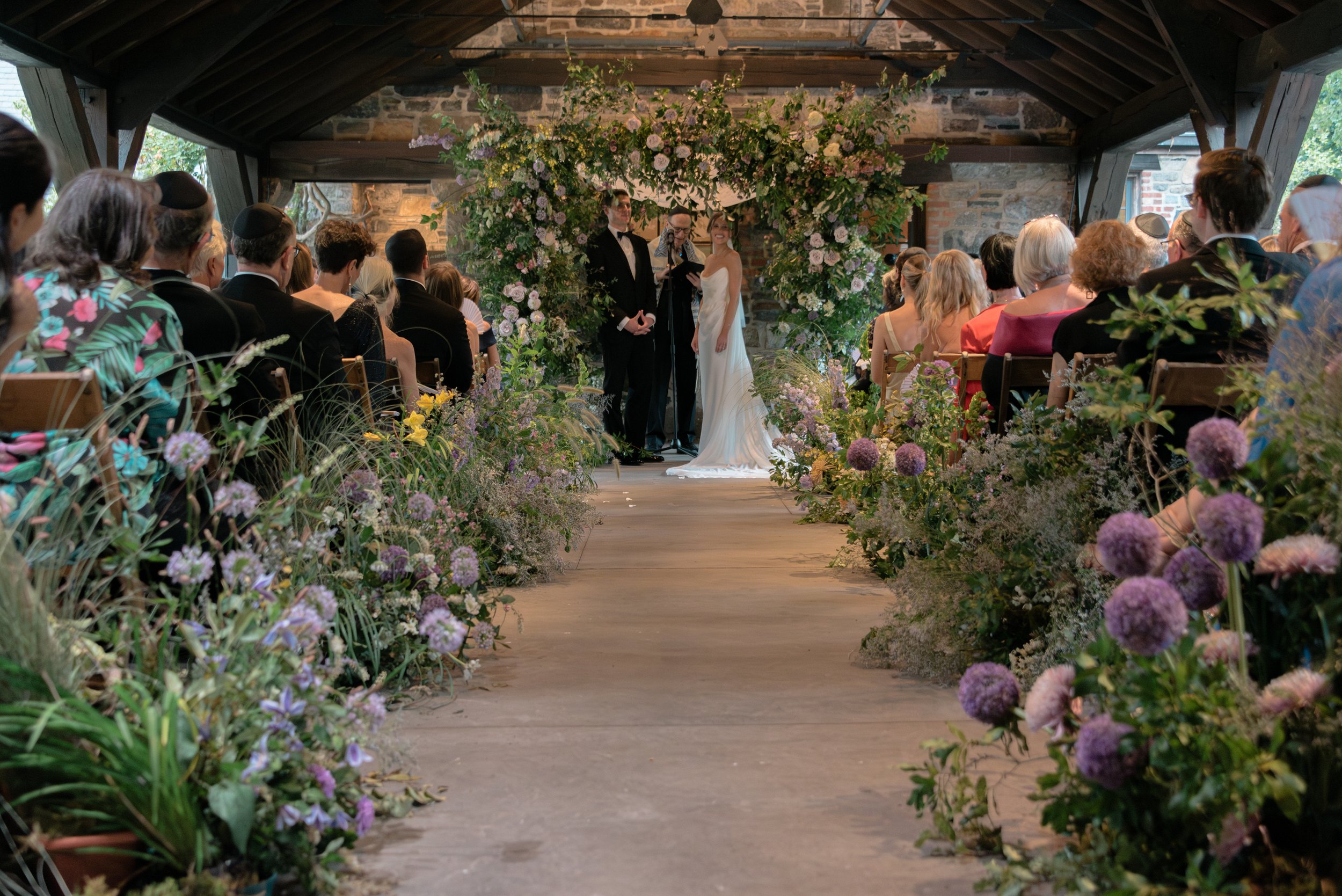 Jennie and Will look out at their guests at their floral-filled ceremony space beneath the pergola in the courtyard at Blue Hill at Stone Barns