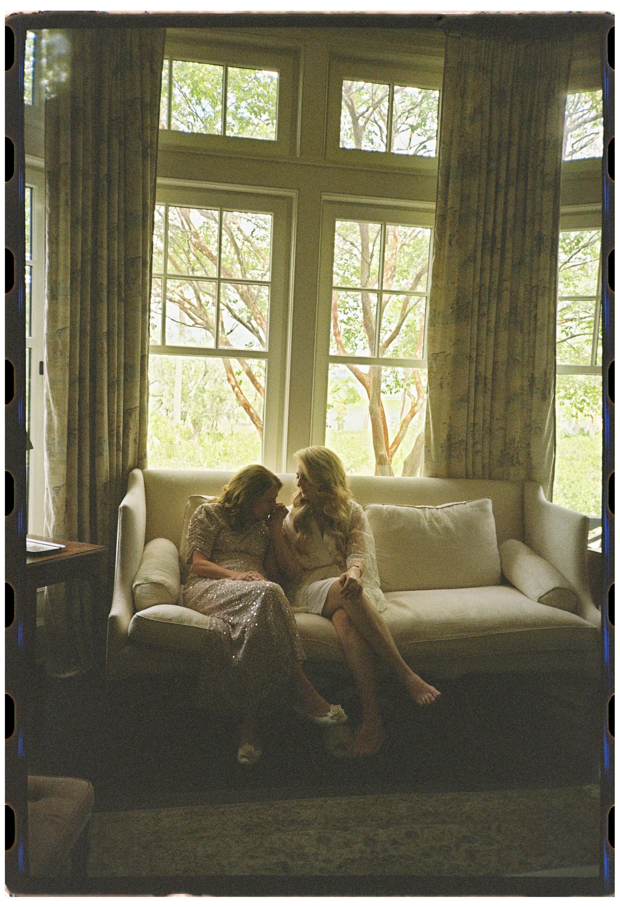 The mother of the bride and the bride share a quiet conversation in window light while preparing for the wedding at a private estate on Kiawah Island.
