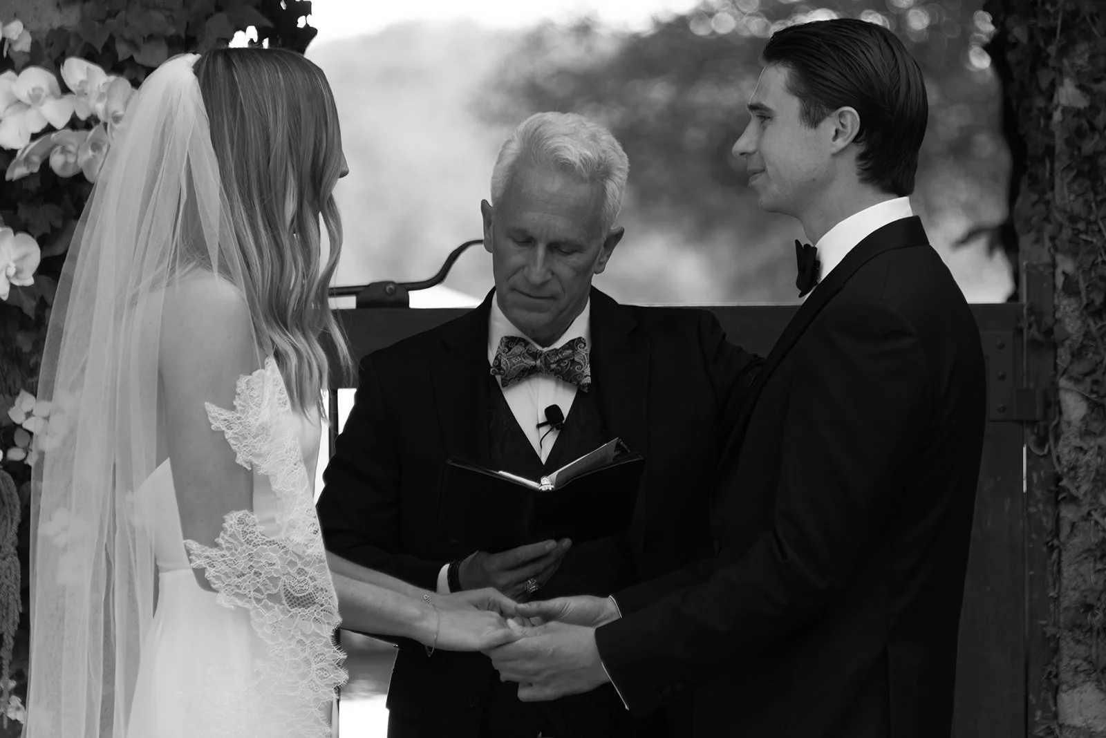 Black-and-white photograph of the bride and groom exchanging vows with their officiant at Goodstone Inn.