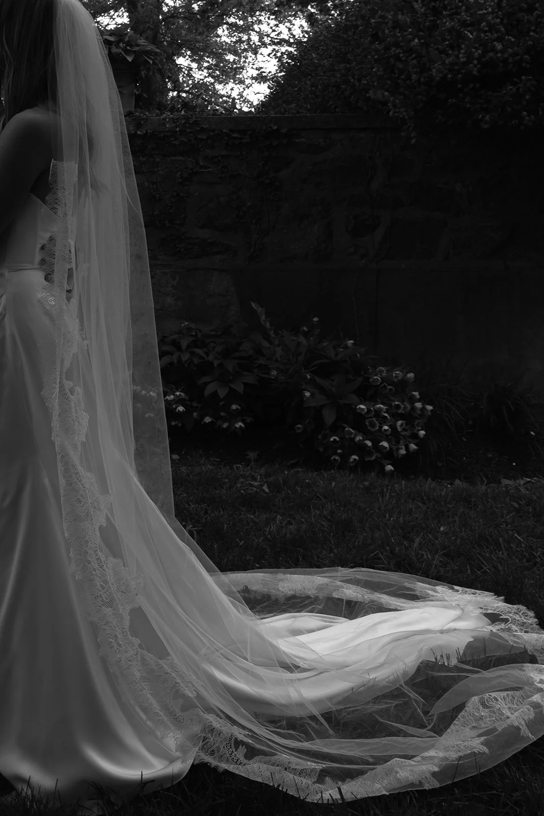 Black-and-white photograph of the bride’s cathedral veil flowing behind her in the gardens at Goodstone Inn.