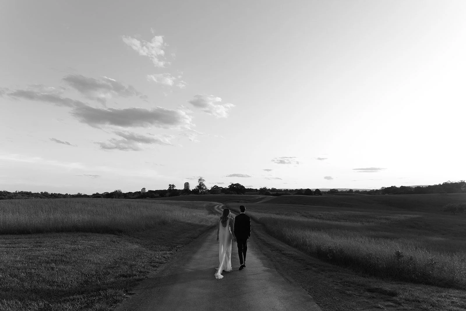 Black-and-white wide portrait of the bride and groom standing together in the Hayfield at Goodstone Inn.