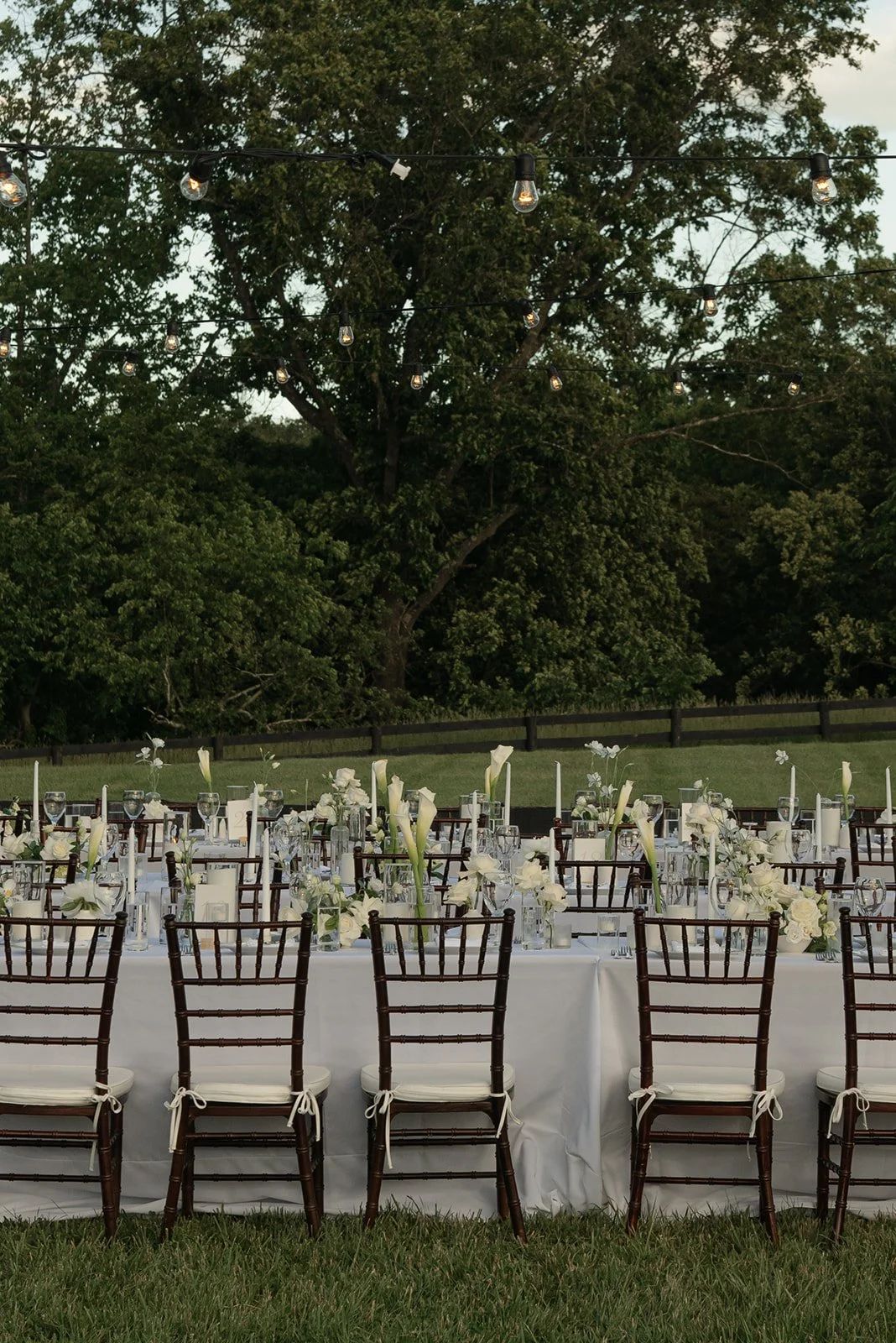 Rows of dark wooden dining chairs and long white tables set outdoors beneath trees at Goodstone Inn.