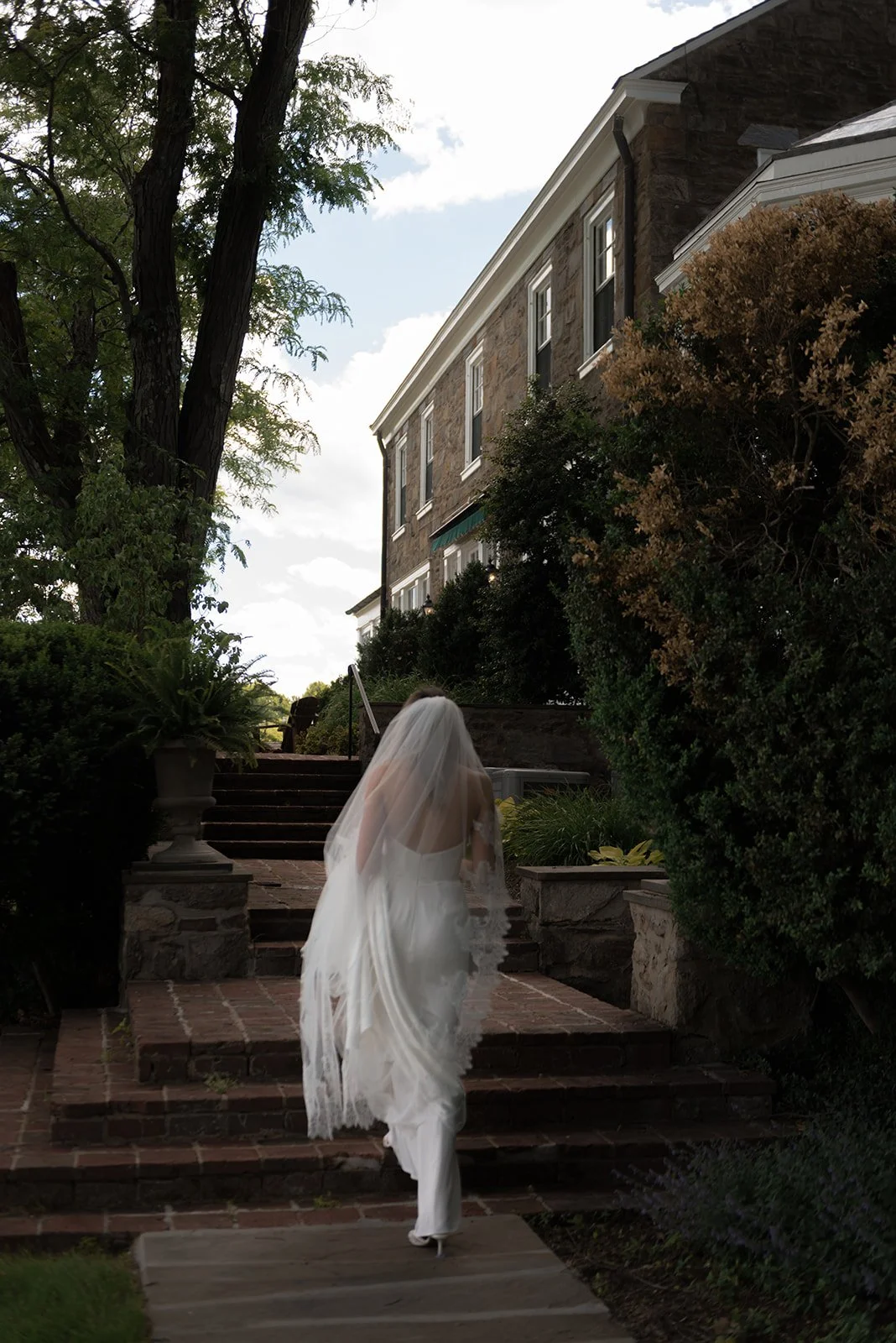 Bride walking along the exterior of the Manor House in her Tara Lauren Bridal wedding gown at Goodstone Inn.