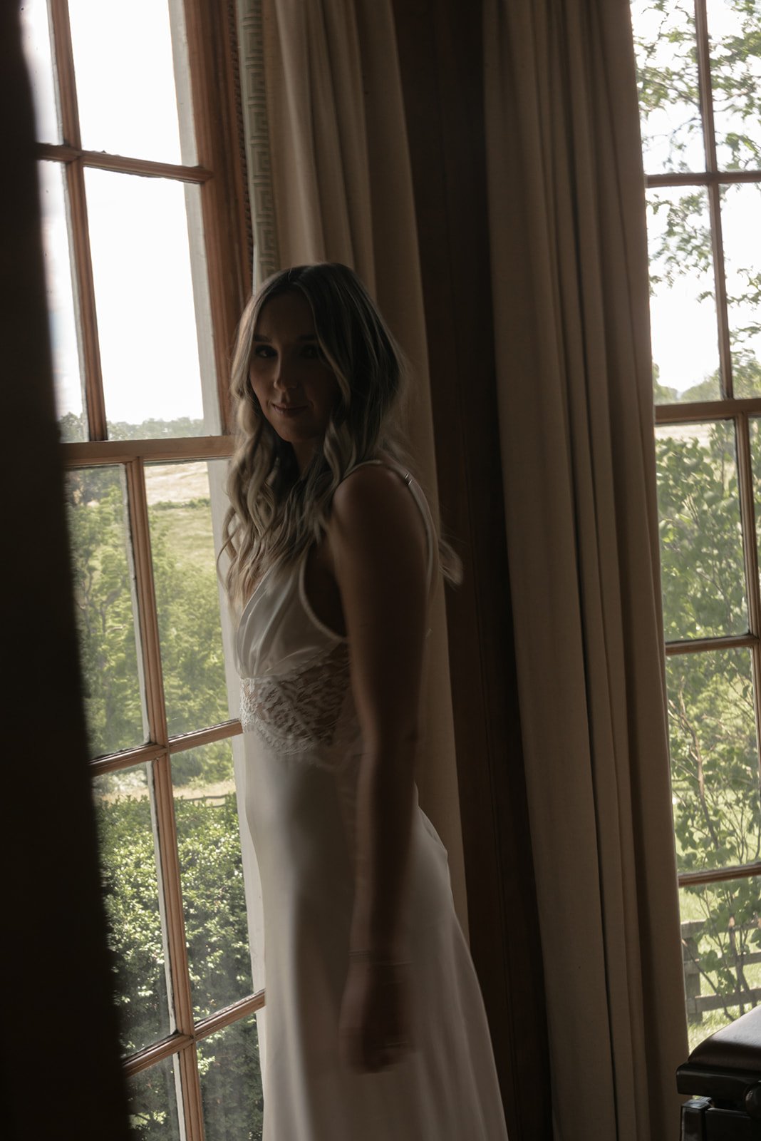 Bride standing beside a bright window inside the Manor House at Goodstone Inn.