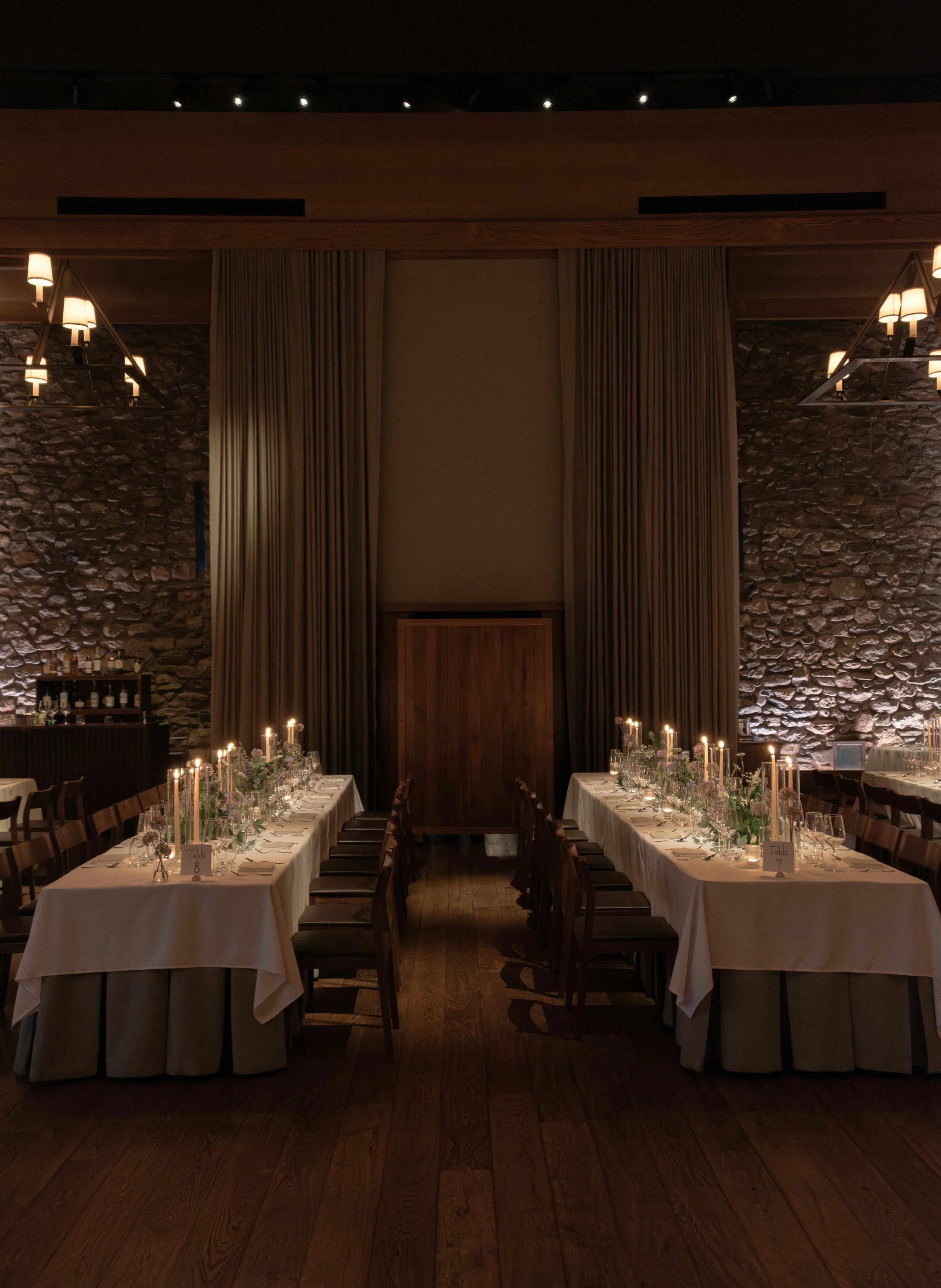 Symmetrical view of the candlelit wedding dining room at Blue Hill at Stone Barns with long tables designed by Mudari Creative.